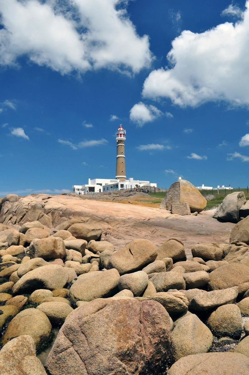 Lighthouse on a rocky coastline beneath a bright blue sky with white clouds