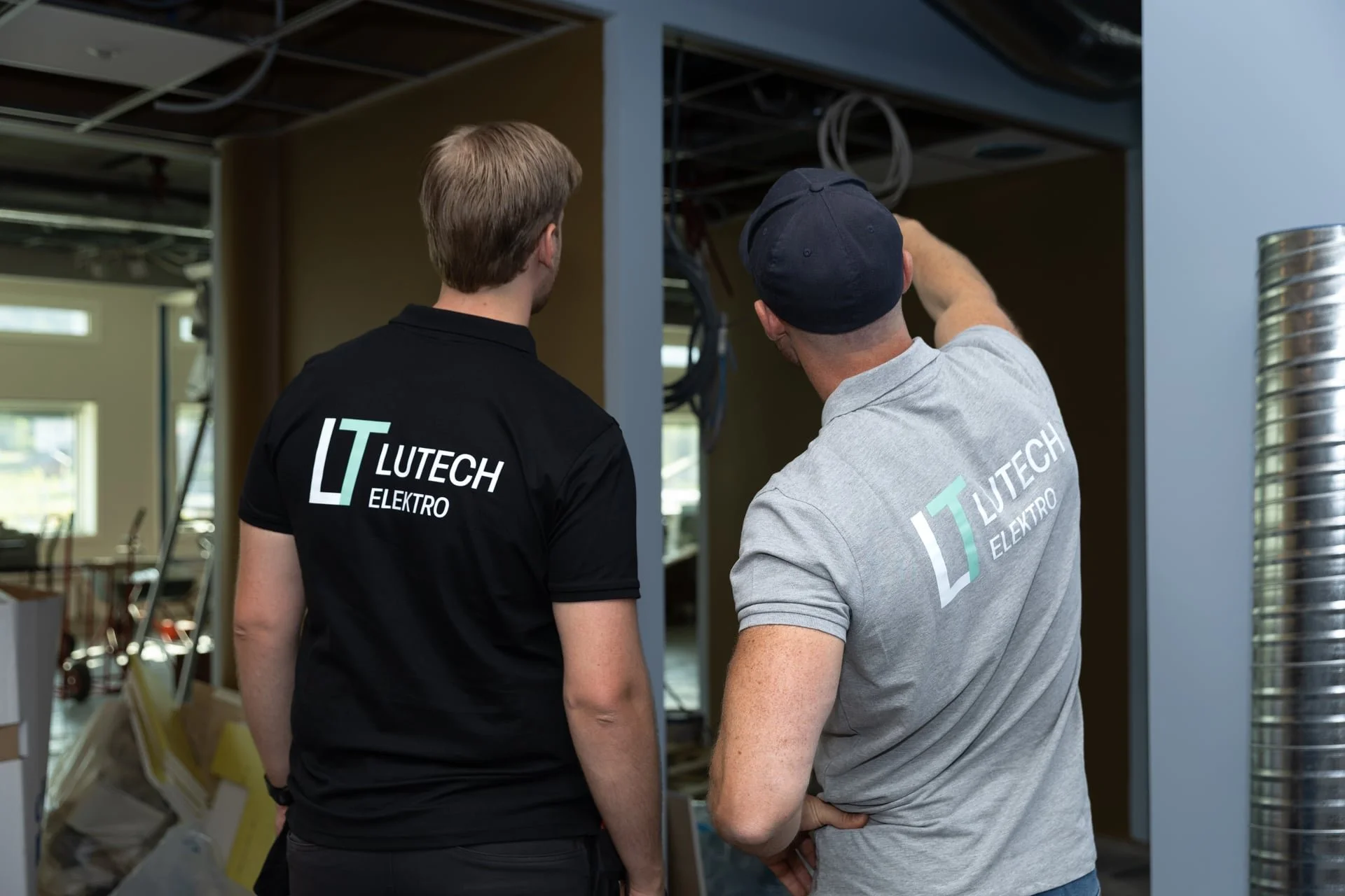 To montører tar en titt på el-installasjon i en byggeprosess, begge med tekst og logo som sier 'Lutech Elektro' på ryggen.