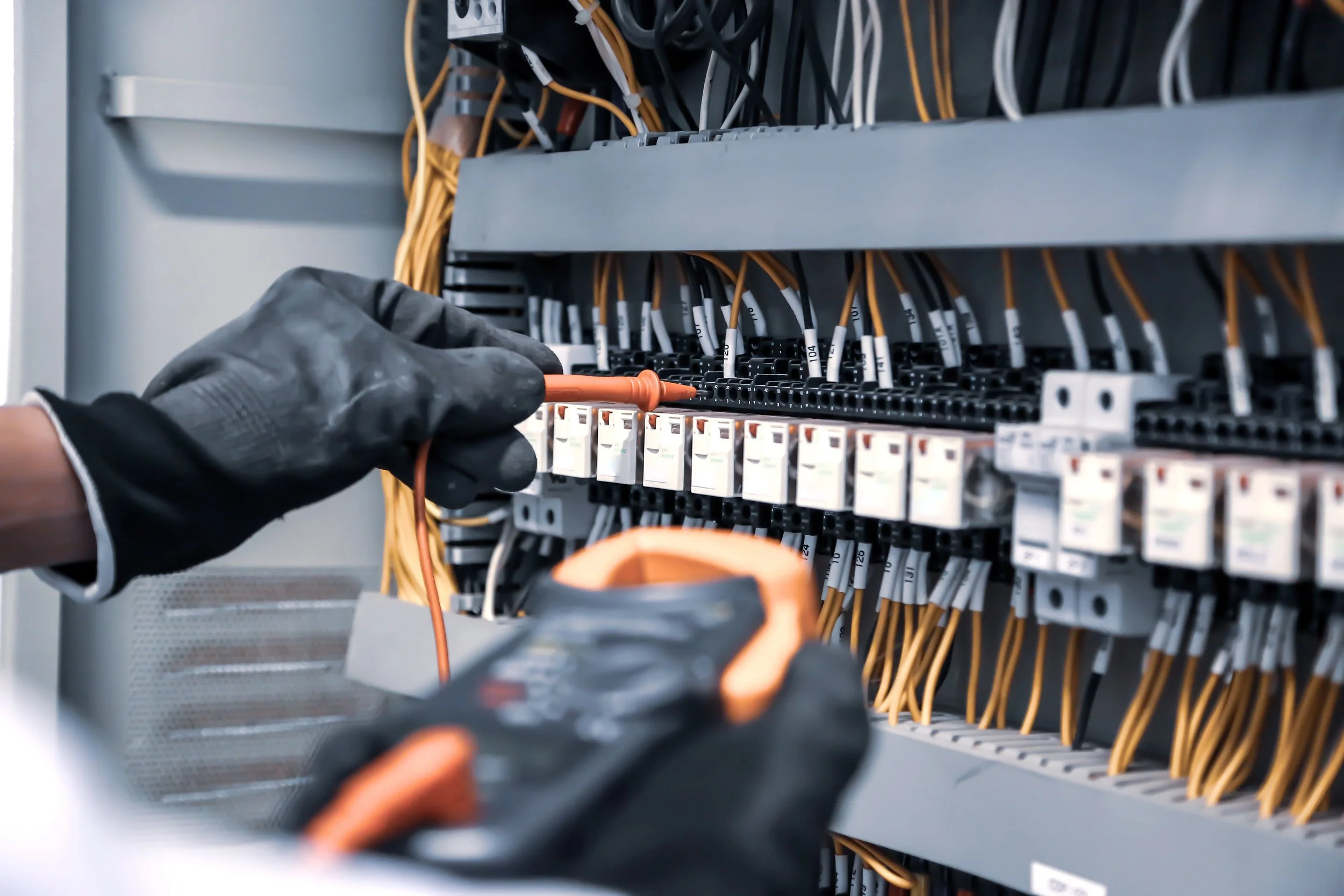 En person i hansker jobber med elektriske ledninger i et elskap.
