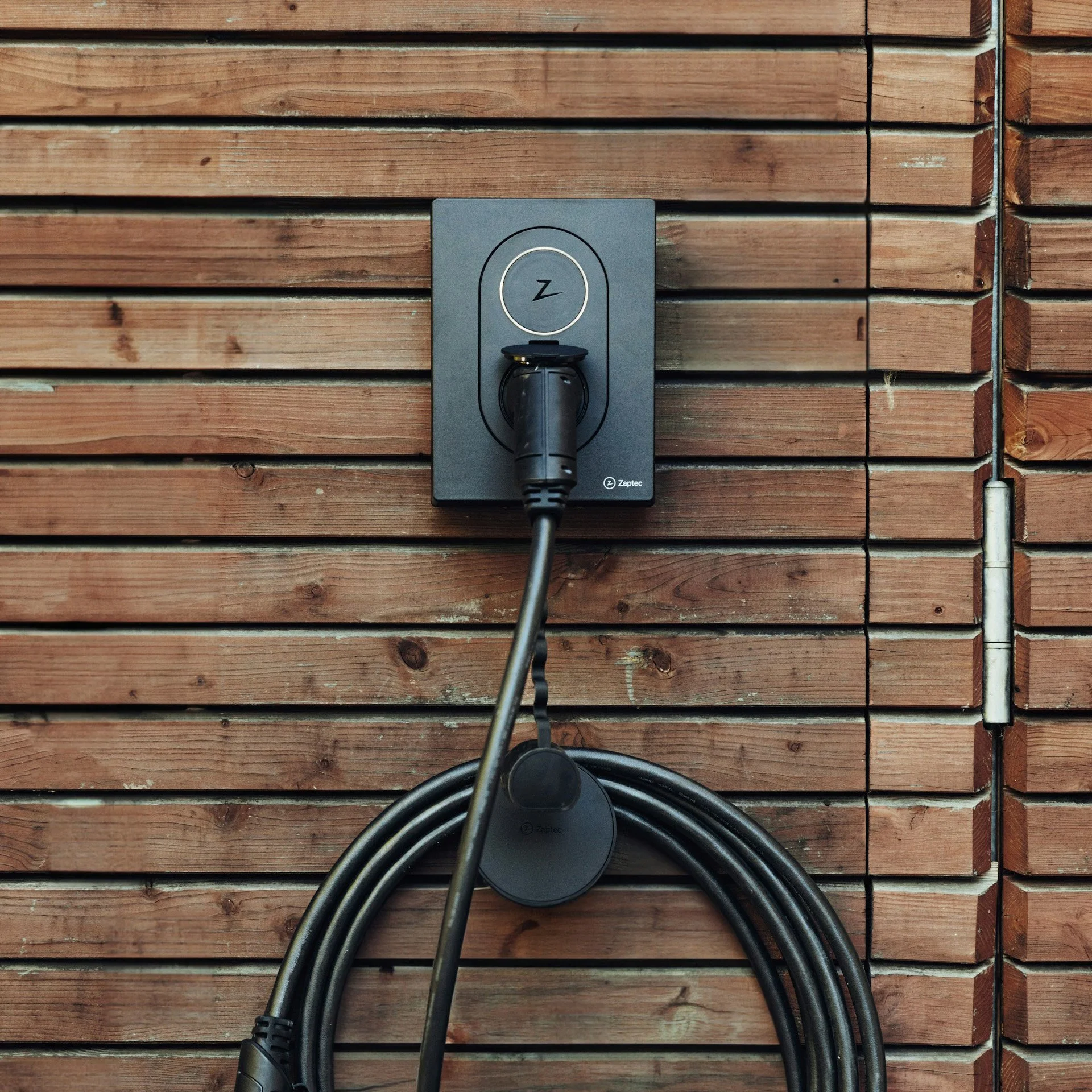 Kabel koblet til en ladeboks montert på en trevegg.
