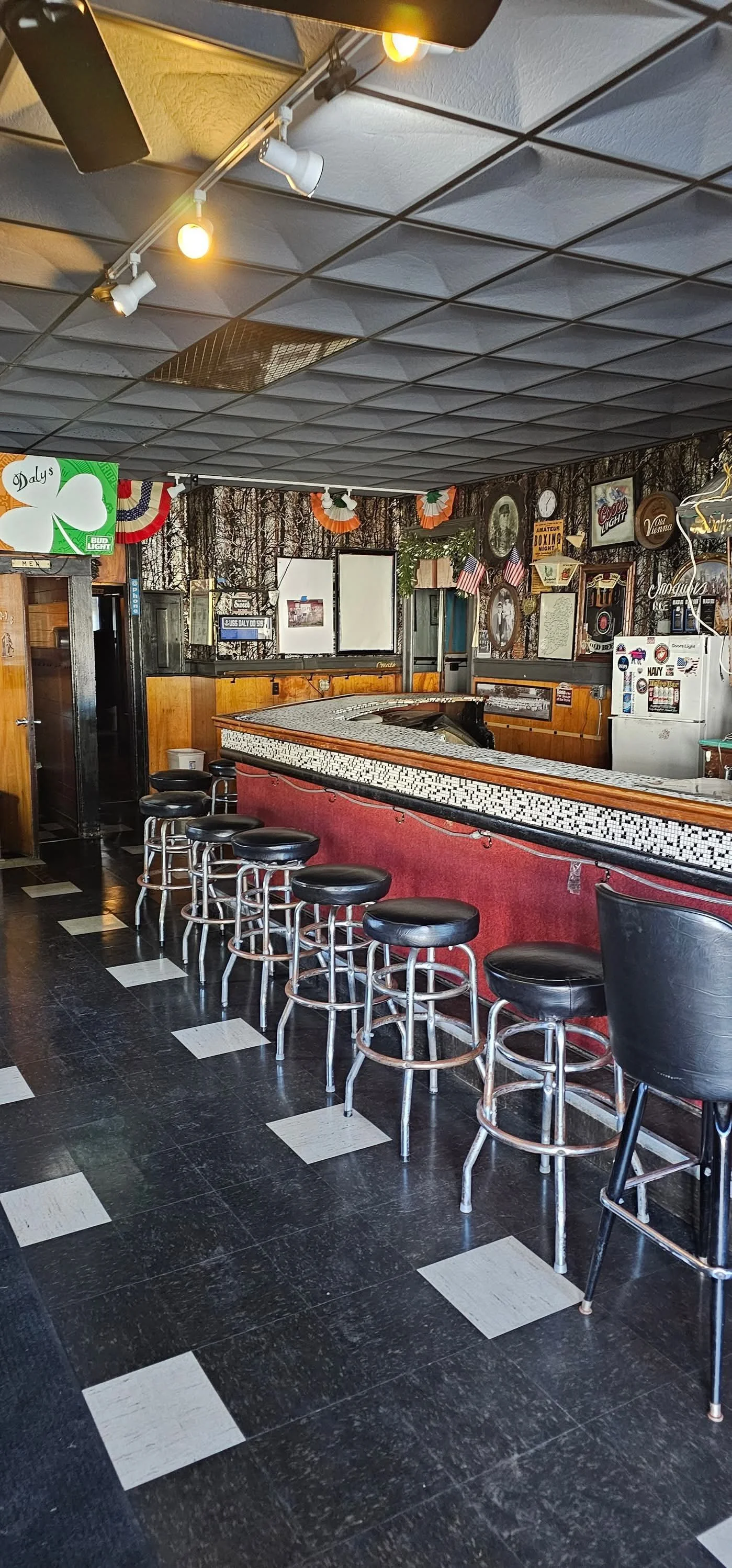 Interior of a bar or pub with a counter, black and white checkered floor, vintage decor, and American flags.