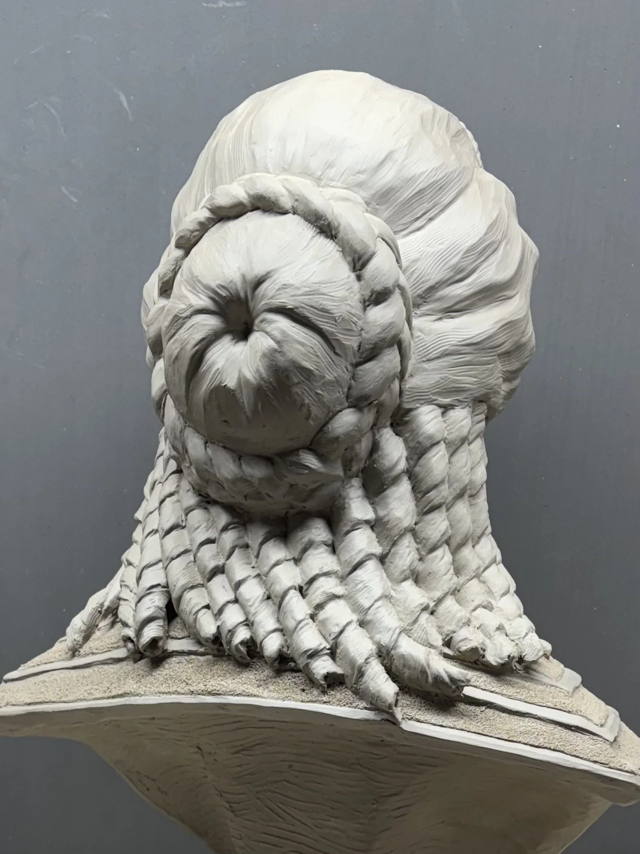 A detailed clay sculpture of a the back of a woman's head with an intricate hair style.  