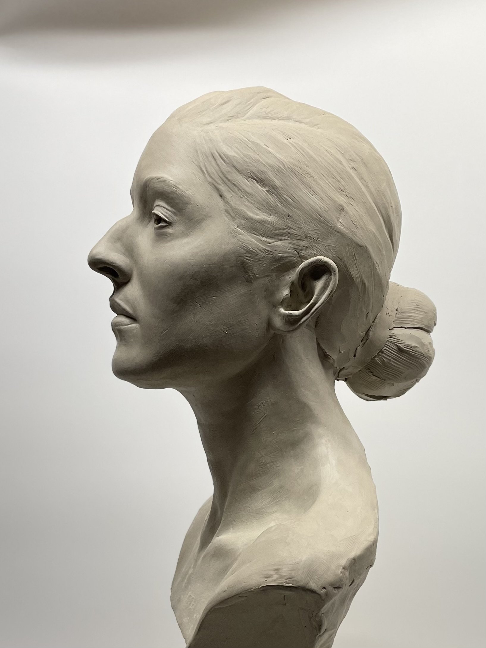 Sculpture of a woman's head in profile with detailed hair and facial features, light-colored, against a plain background.