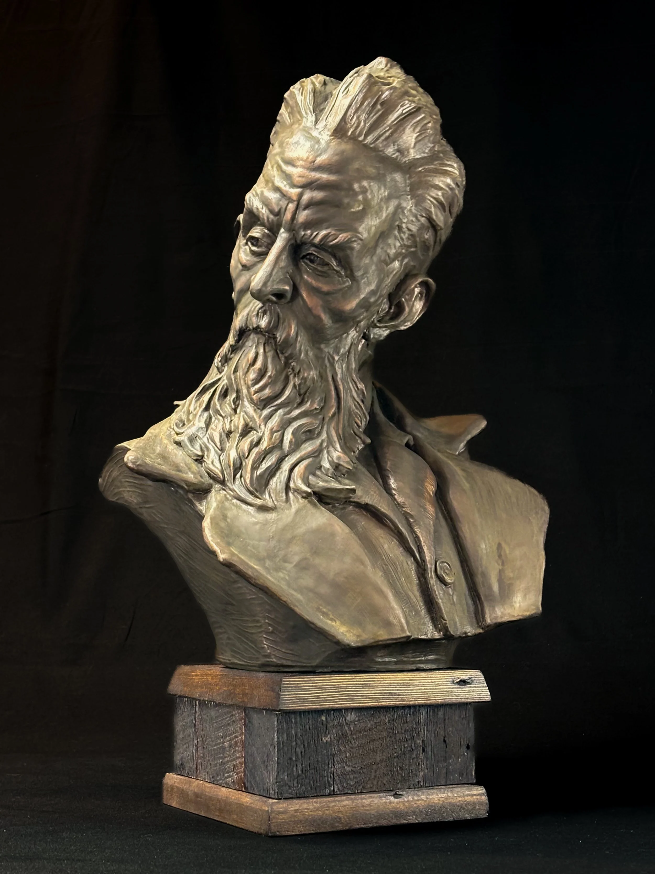 Bronze bust of abolitionist John Brown, a bearded man with detailed facial features, wearing a collared shirt, displayed on a wooden base against a dark background.