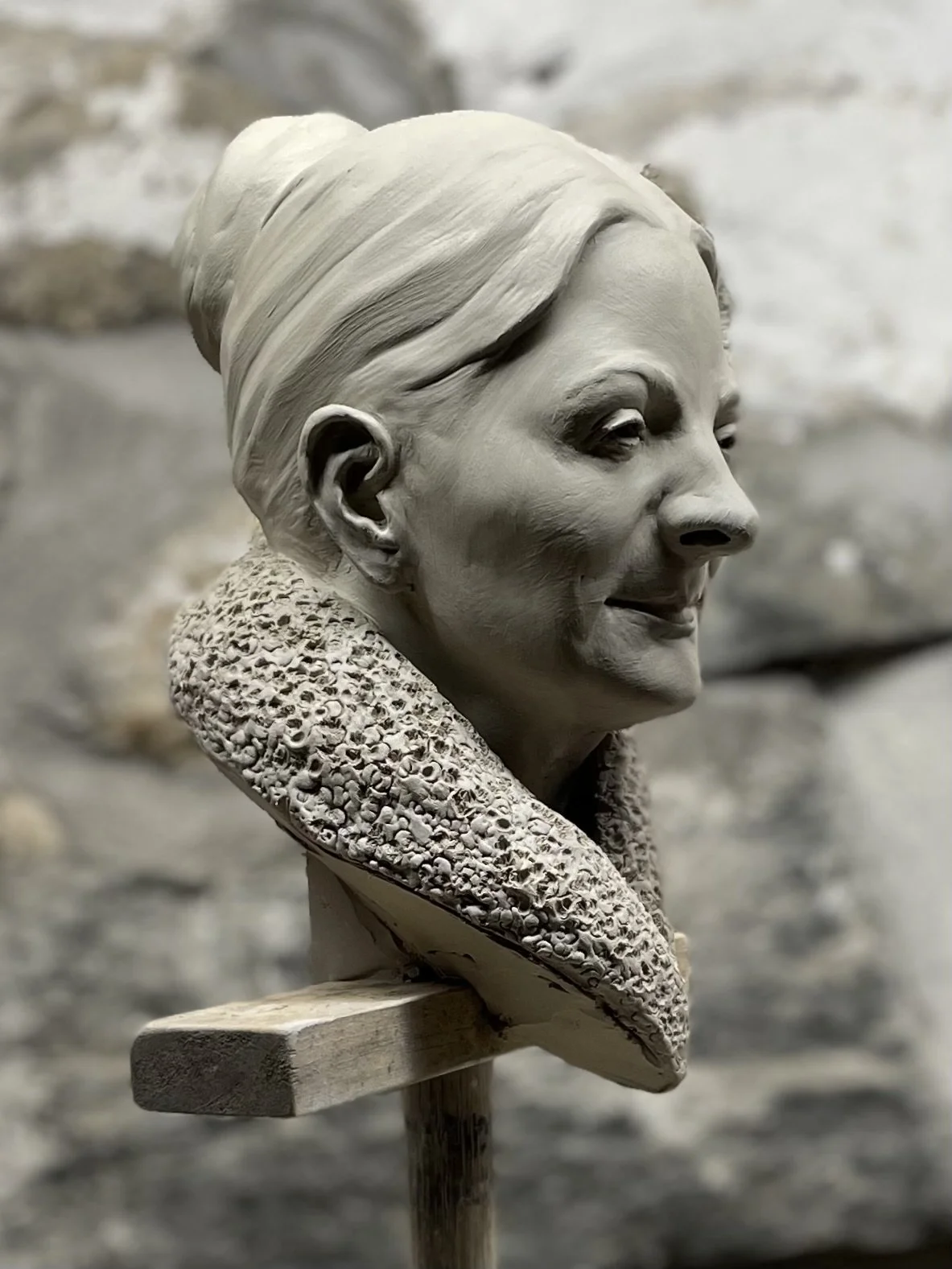 A detailed ceramic bust sculpture of a woman wearing a textured scarf around her neck.