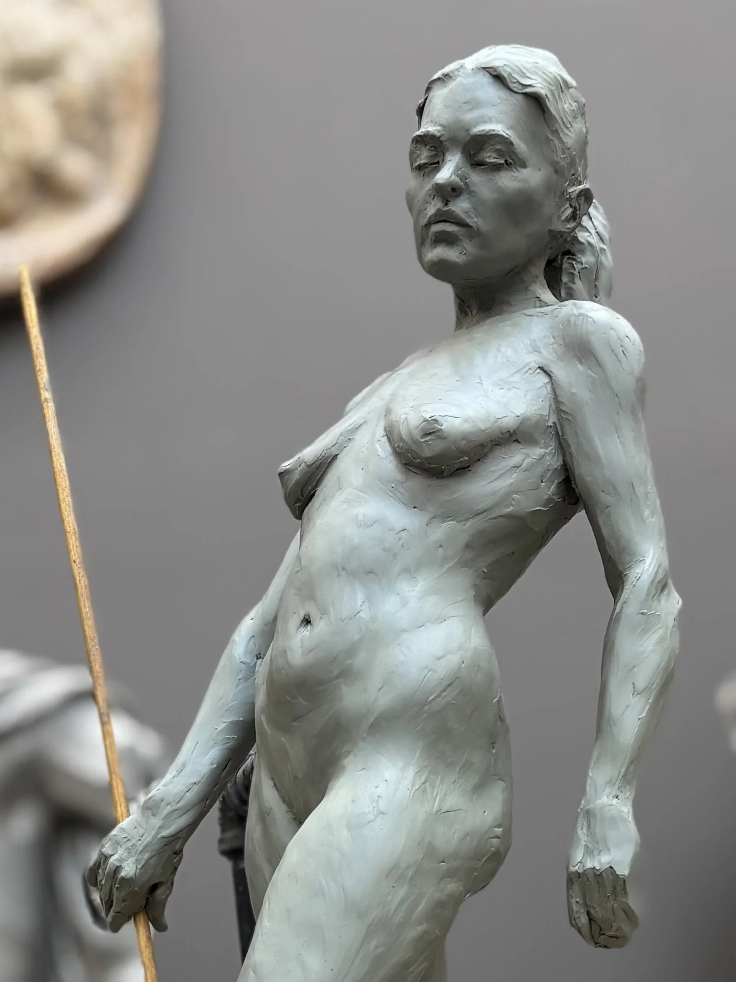 Close-up of a white sculpture of a nude woman with her eyes closed, featuring realistic facial features and detailed hair, against a plain background.