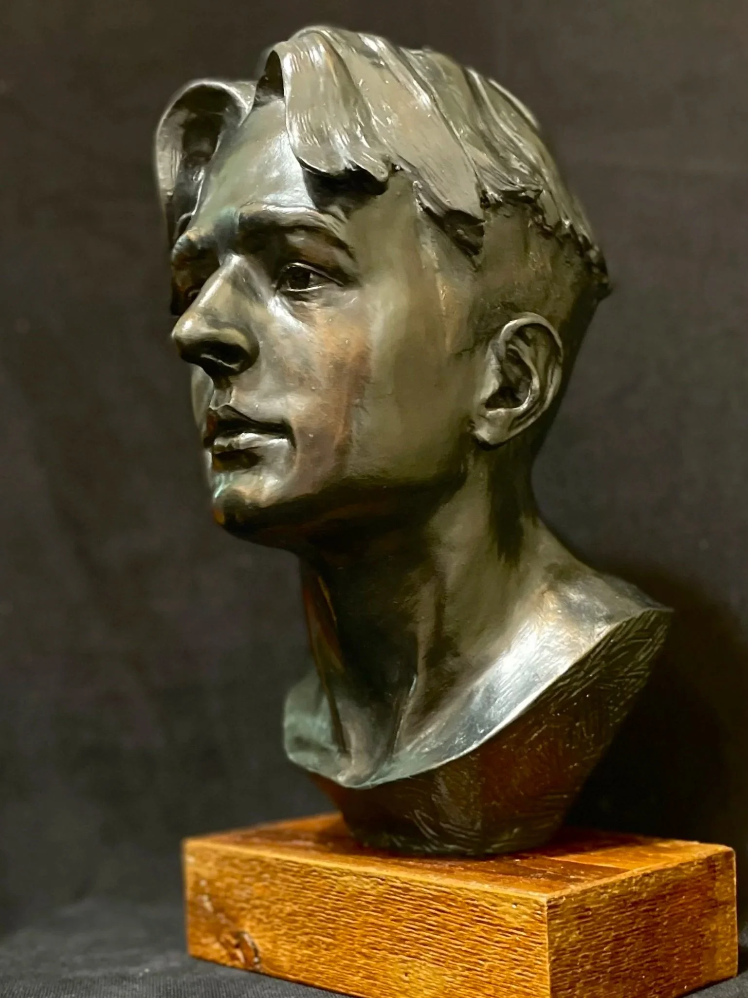 A clay sculpture of a person's head, positioned on a wooden base against a dark background.