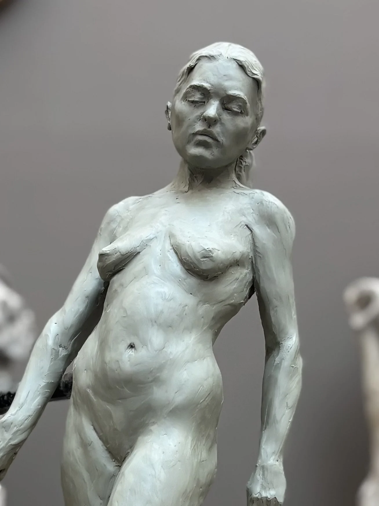 A monochrome sculpture of a nude woman with her eyes closed and head tilted slightly to the side.