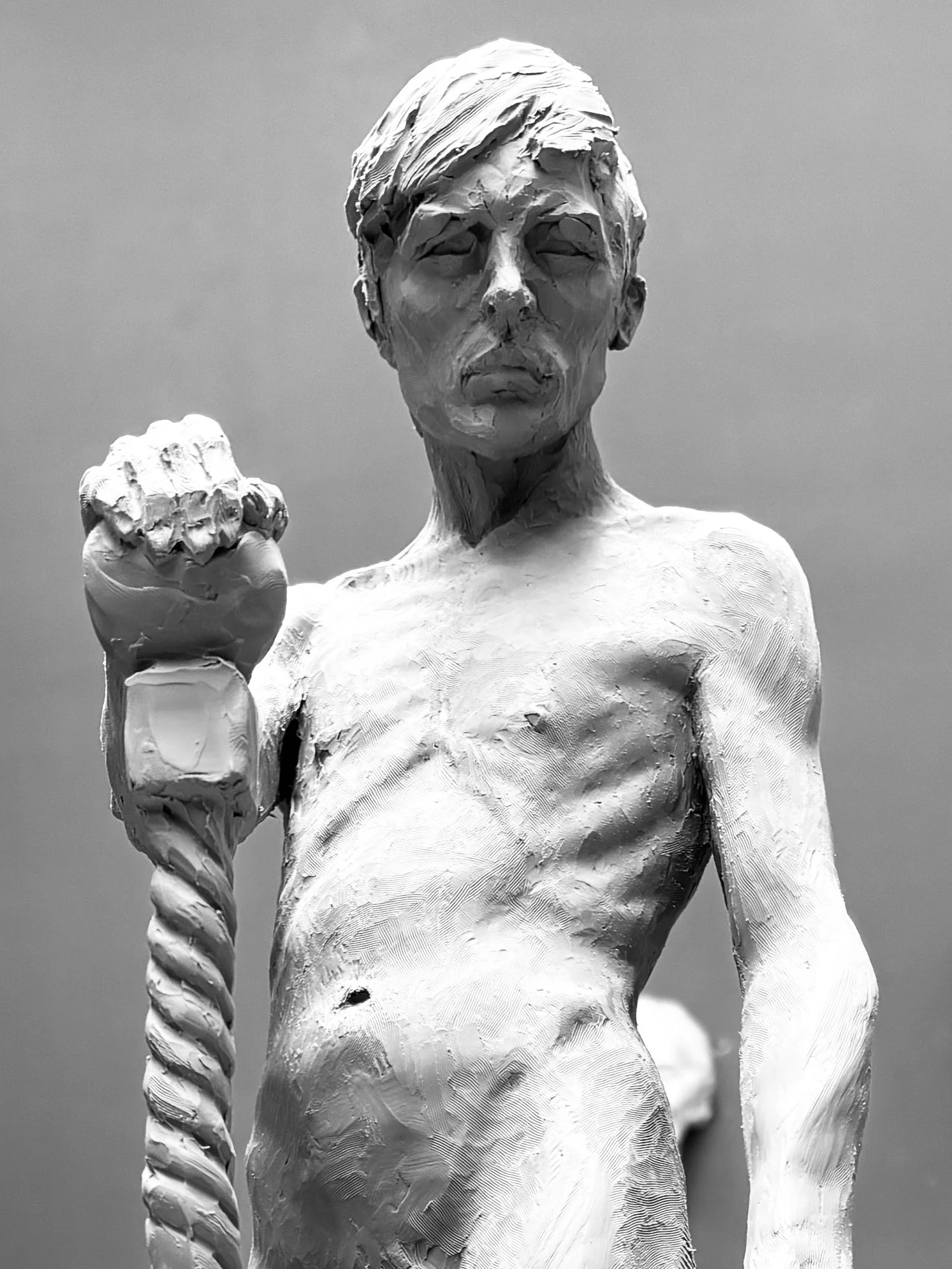Black and white sculpture of a man with short hair, holding a small object in his clenched fist, with a serious expression.