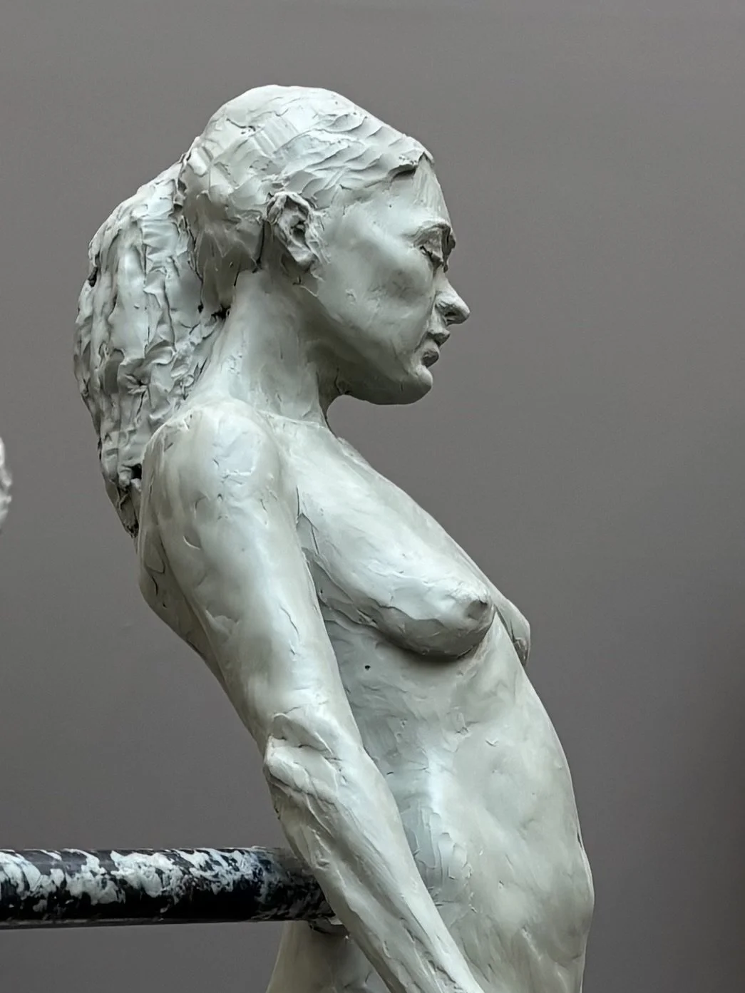 Sculpture of a woman with naked upper body and shoulder-length hair, facing right, with realistic details.