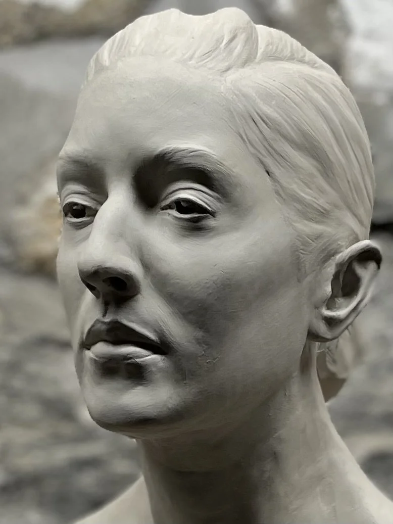 A close-up sculpture of a woman's face in grayscale with detailed facial features and hair texture.