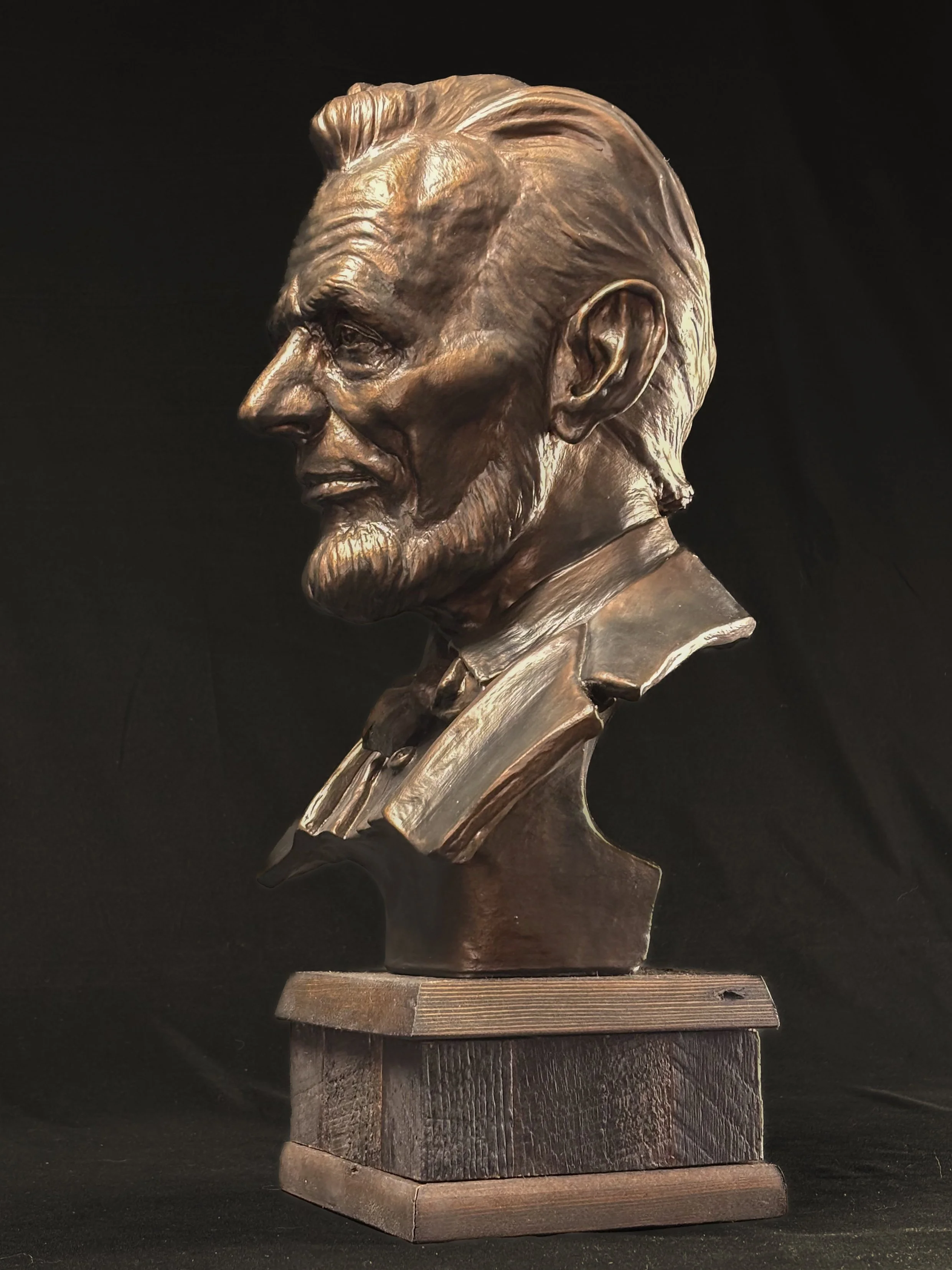Bronze bust sculpture of Abraham Lincoln, wearing a suit, on a wooden base.