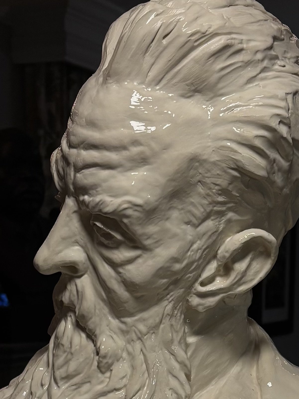 Close-up of a detailed clay sculpture of an elderly man's face in profile, showing wrinkles and textured hair.