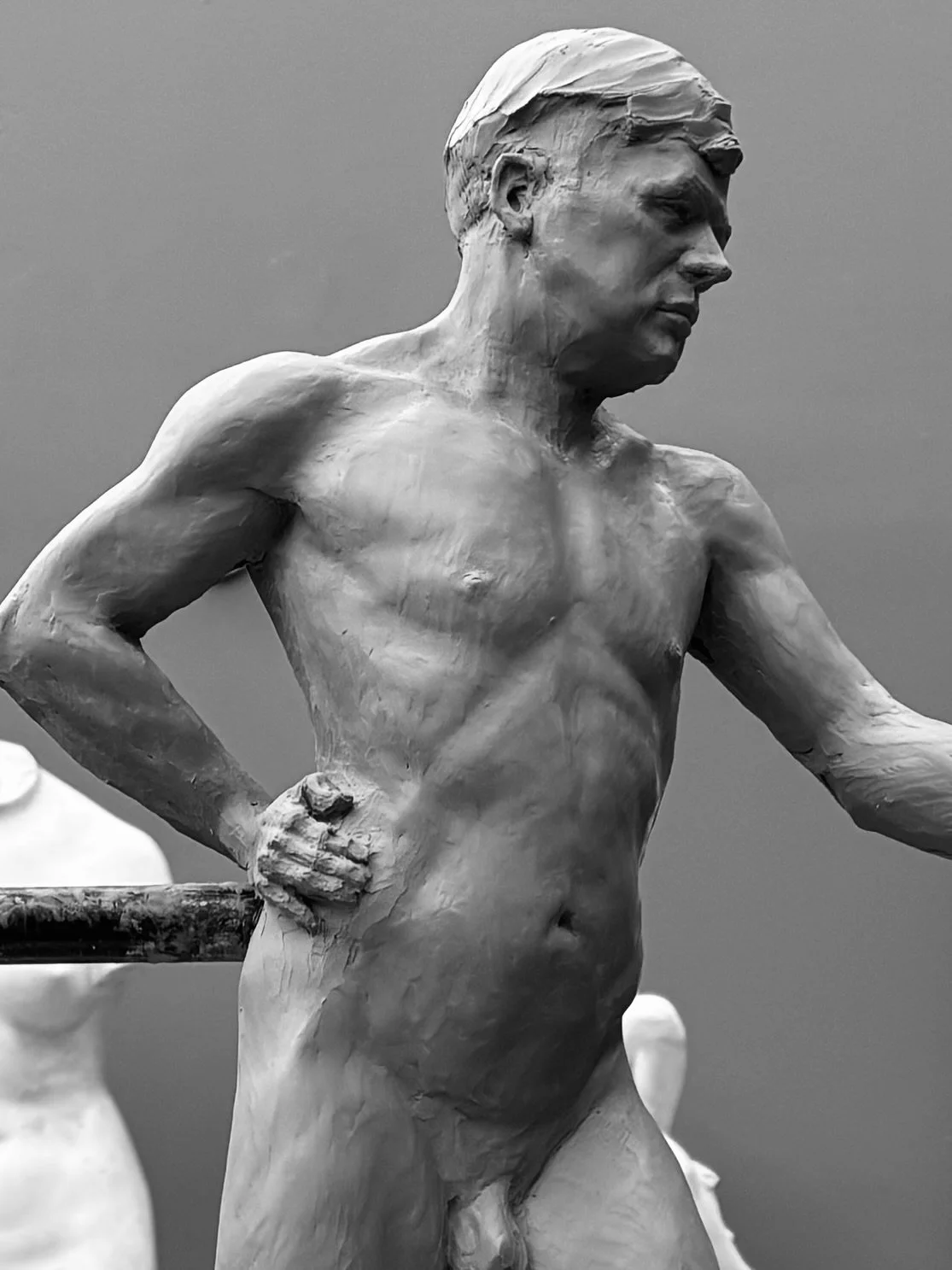 Black-and-white photograph of a sculpture of a nude man with a muscular build, hands on hips, looking downward..