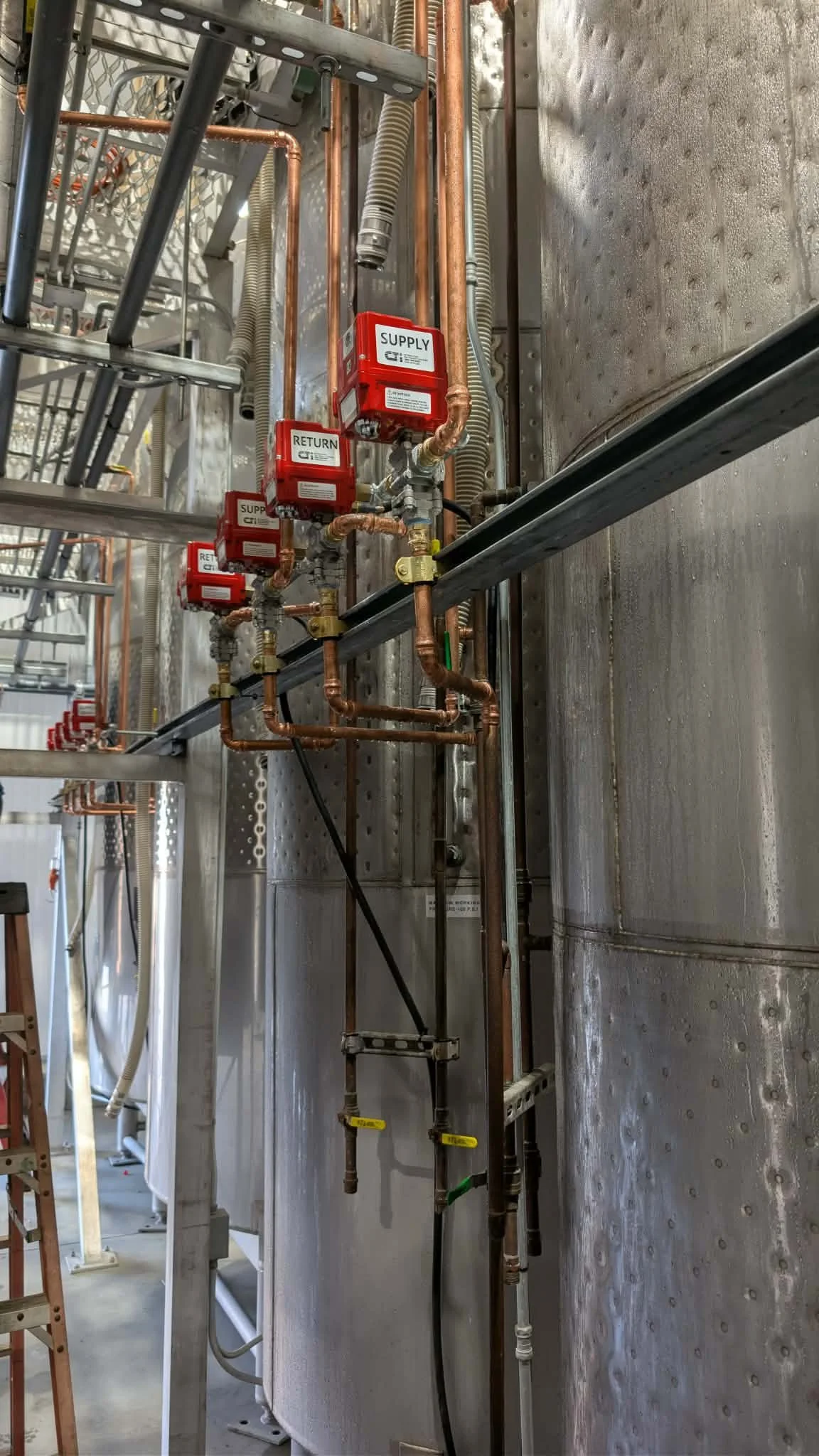Industrial plumbing system with copper pipes and red supply and return valves mounted on a wall.