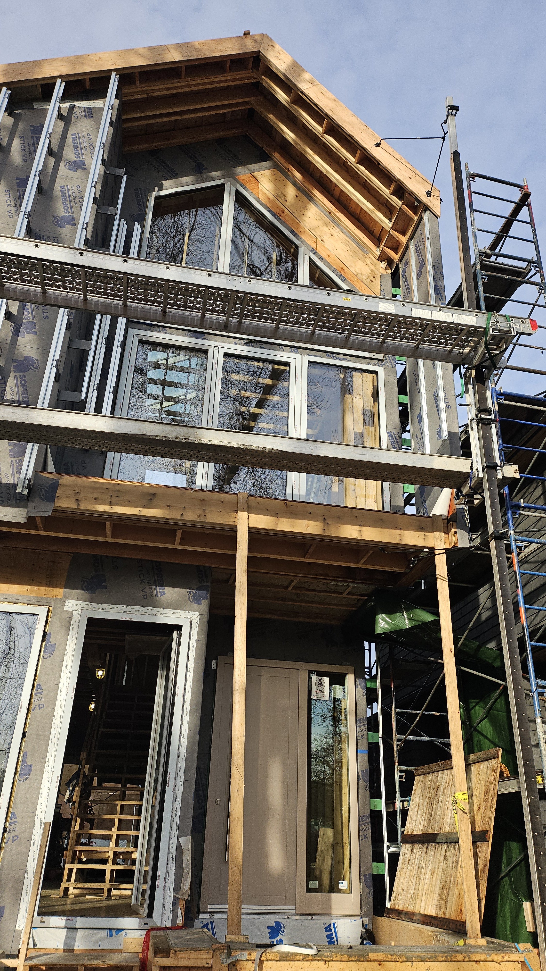 Construction site of a building with exposed framing, windows installed, and scaffolding.