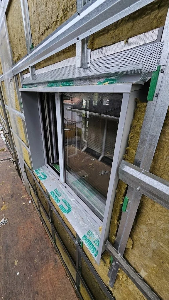 View of a building under construction with an installed window opening, custom flashings, cascadia clips, Z-girts, hat tracks and roxul insulation visible on the exterior wall.