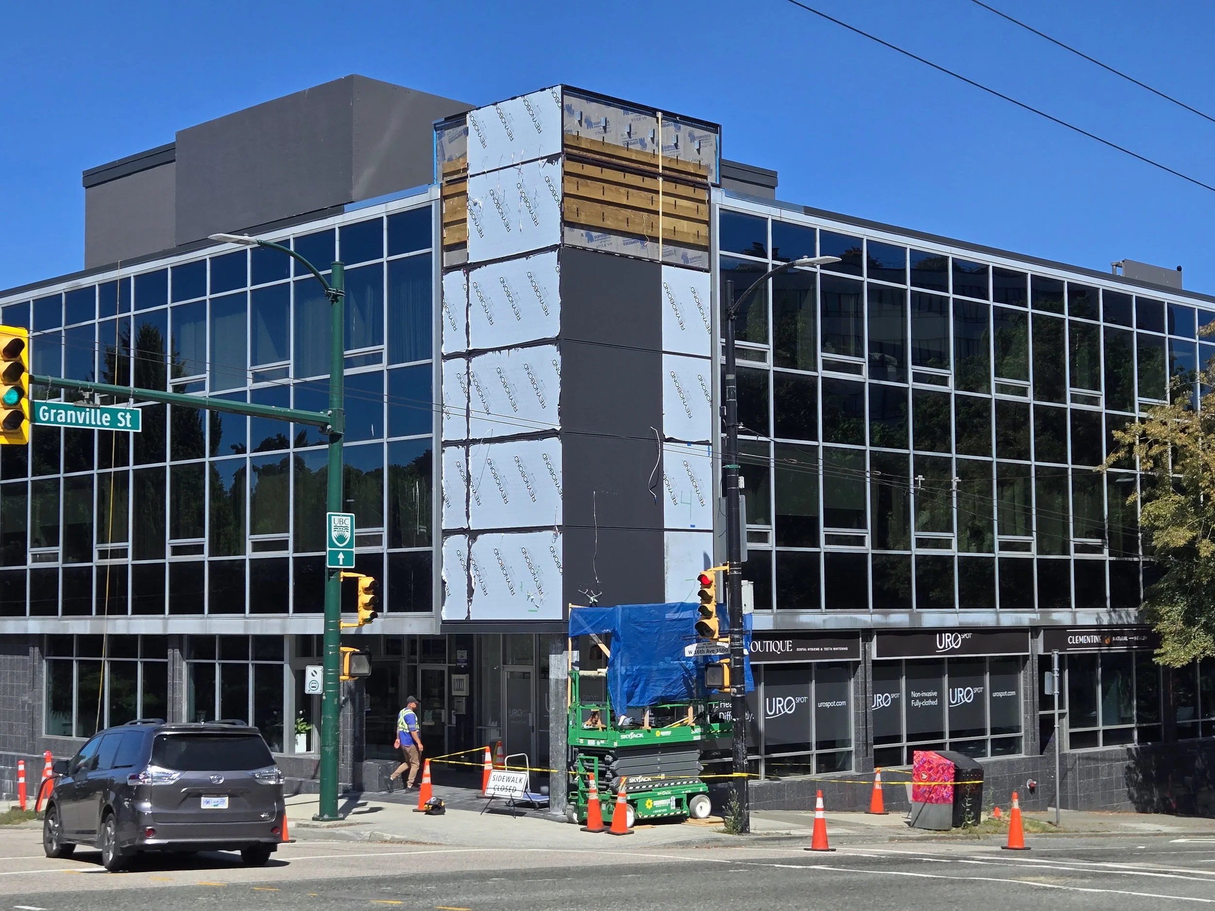 Construction workers and equipment on a city street in front of a modern glass building, with orange cones and a street sign for Granville Street.