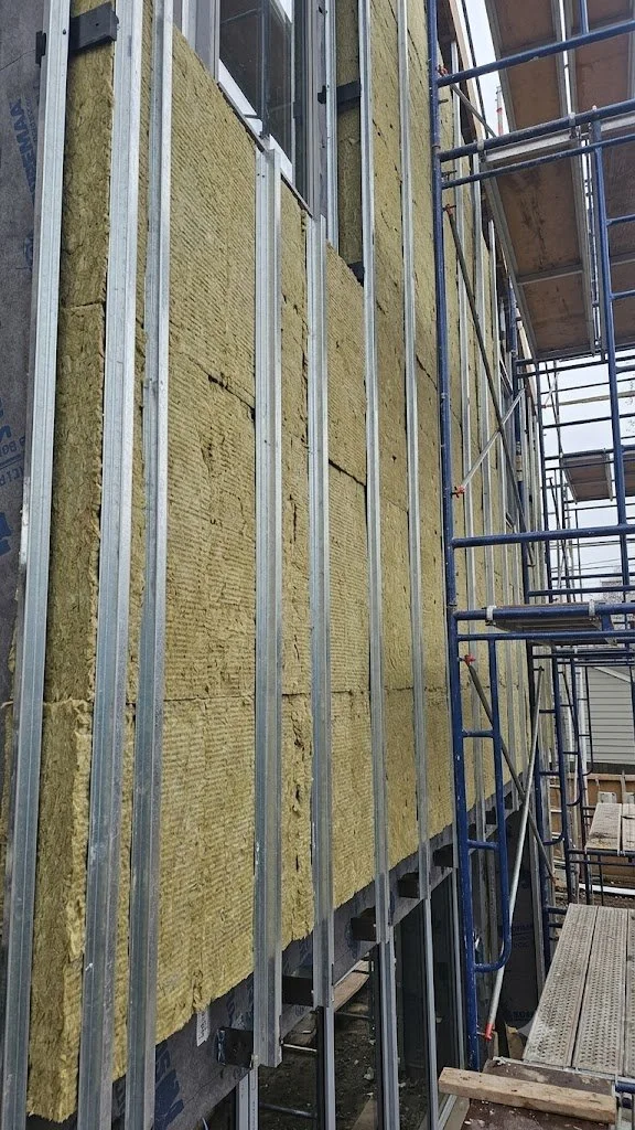 Construction site with building walls sheathed in yellow insulation foam, metal framing, and scaffolding.
