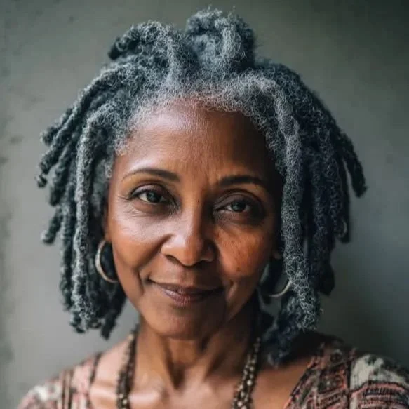 Close-up portrait of an older African American woman with gray dreadlocks, wearing hoop earrings and a patterned top.