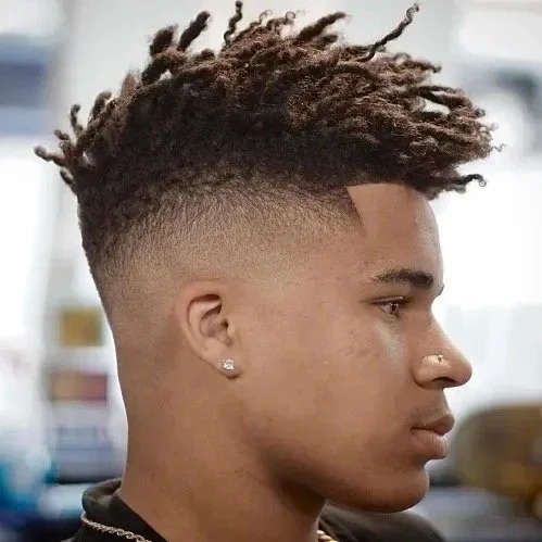 Side profile of a young man with a modern hairstyle, having a fade haircut and long dreadlocks on top.