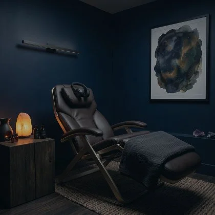 Luxurious massage chair in a modern, dimly lit room with abstract artwork and decorative items on a side table.