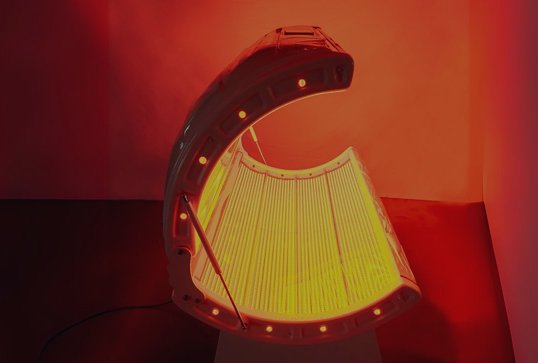 A tanning bed with closed lid emitting a yellow glow in a room with orange and pink walls.