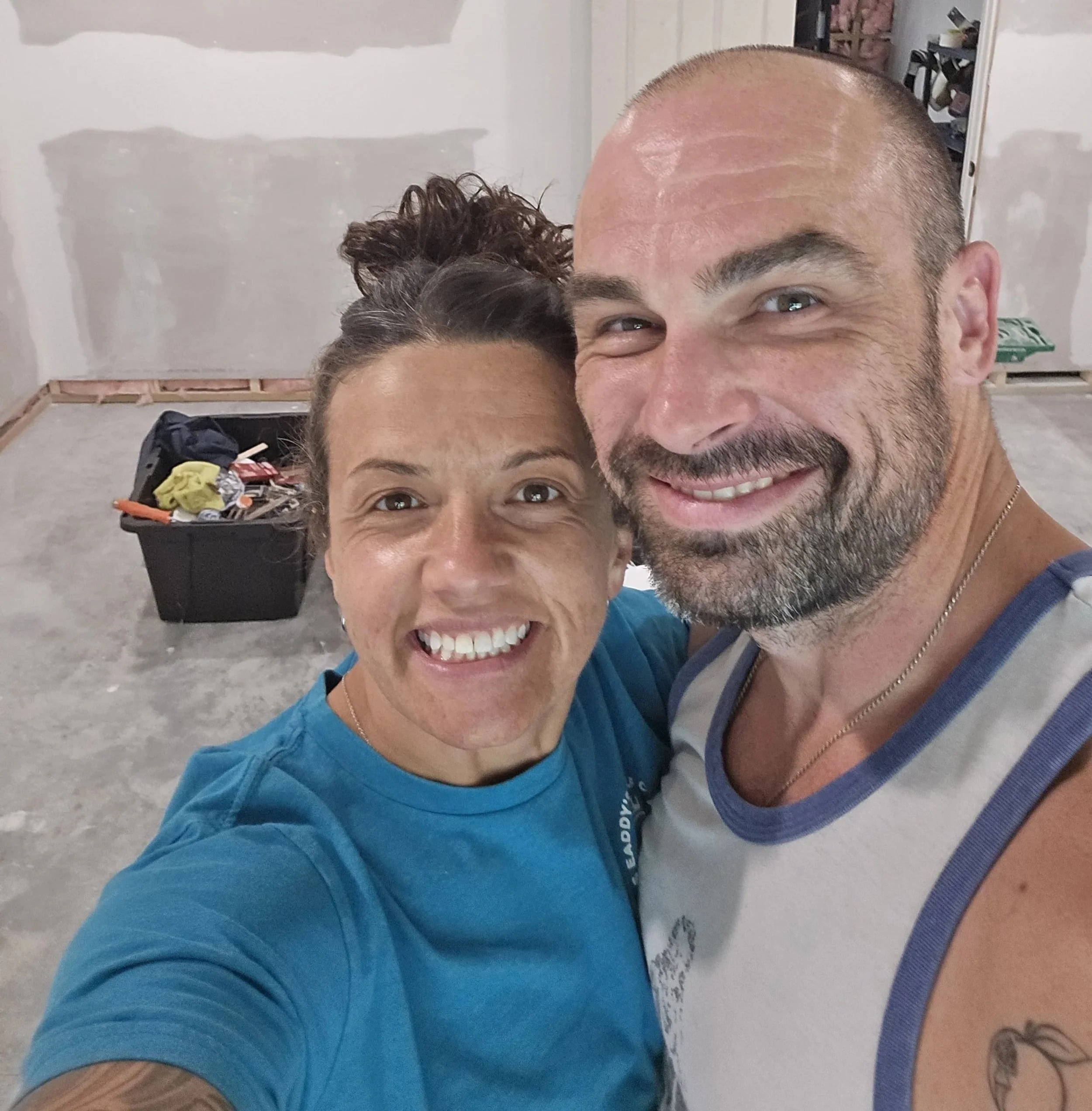 A selfie of a smiling couple taking a photo inside a room under construction with unfinished drywall.