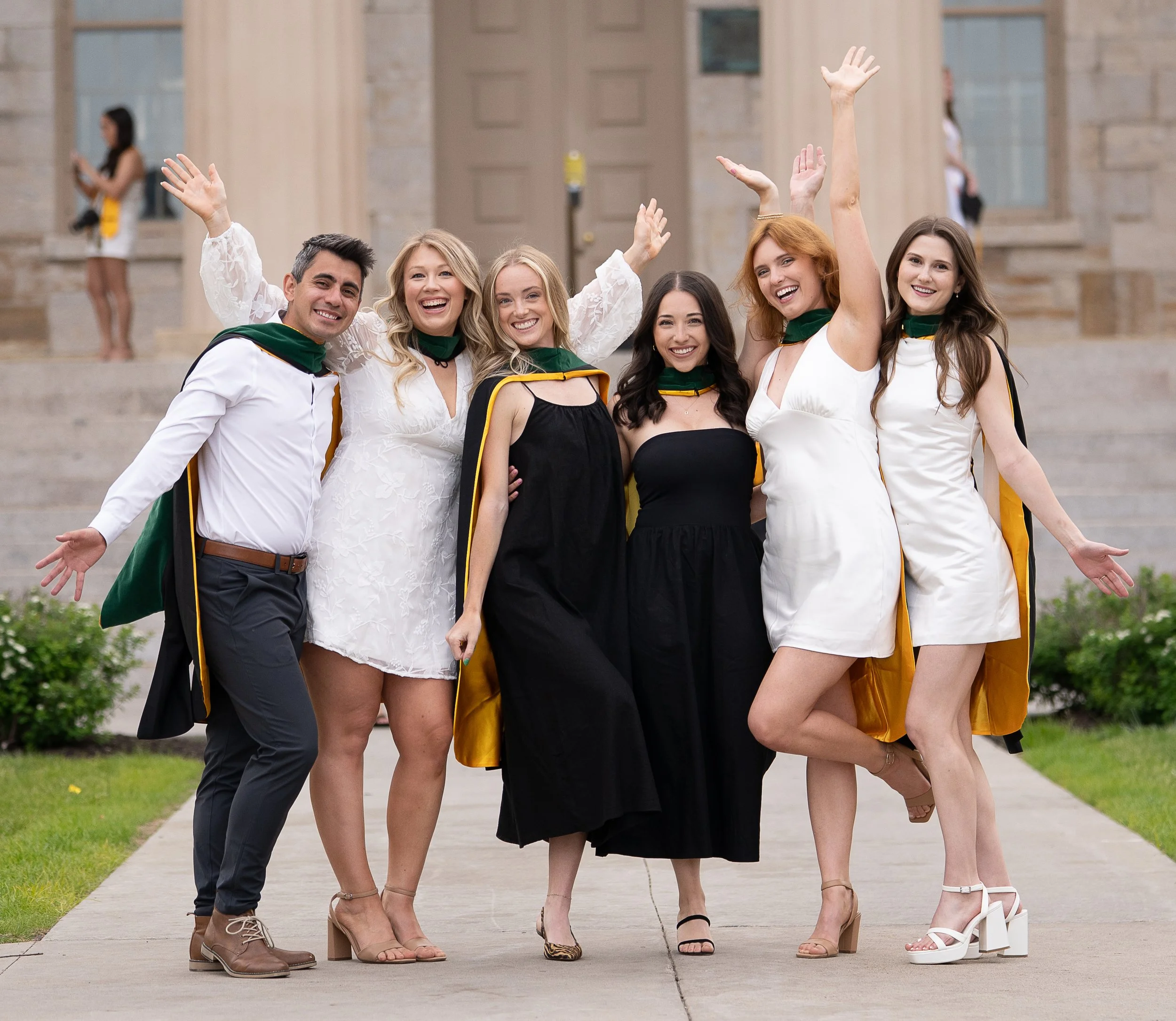 Group of young adults celebrating graduation outdoors, wearing caps and gowns, smiling and posing together.