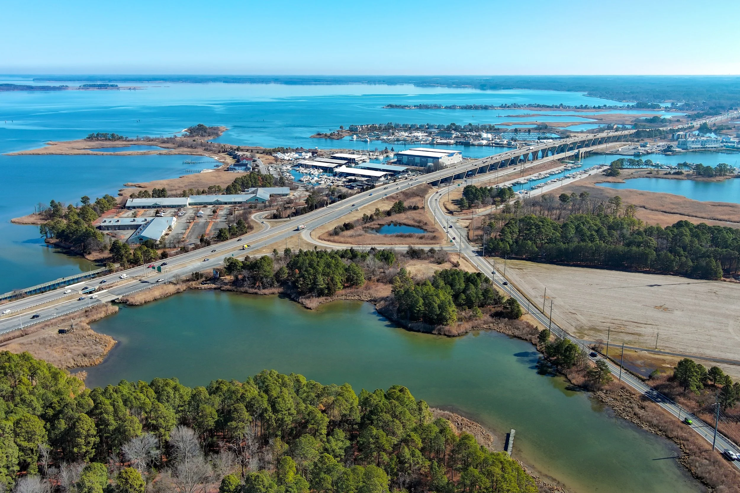 Aerial view of a large body of water with bridges, roads, buildings, and green wooded areas.