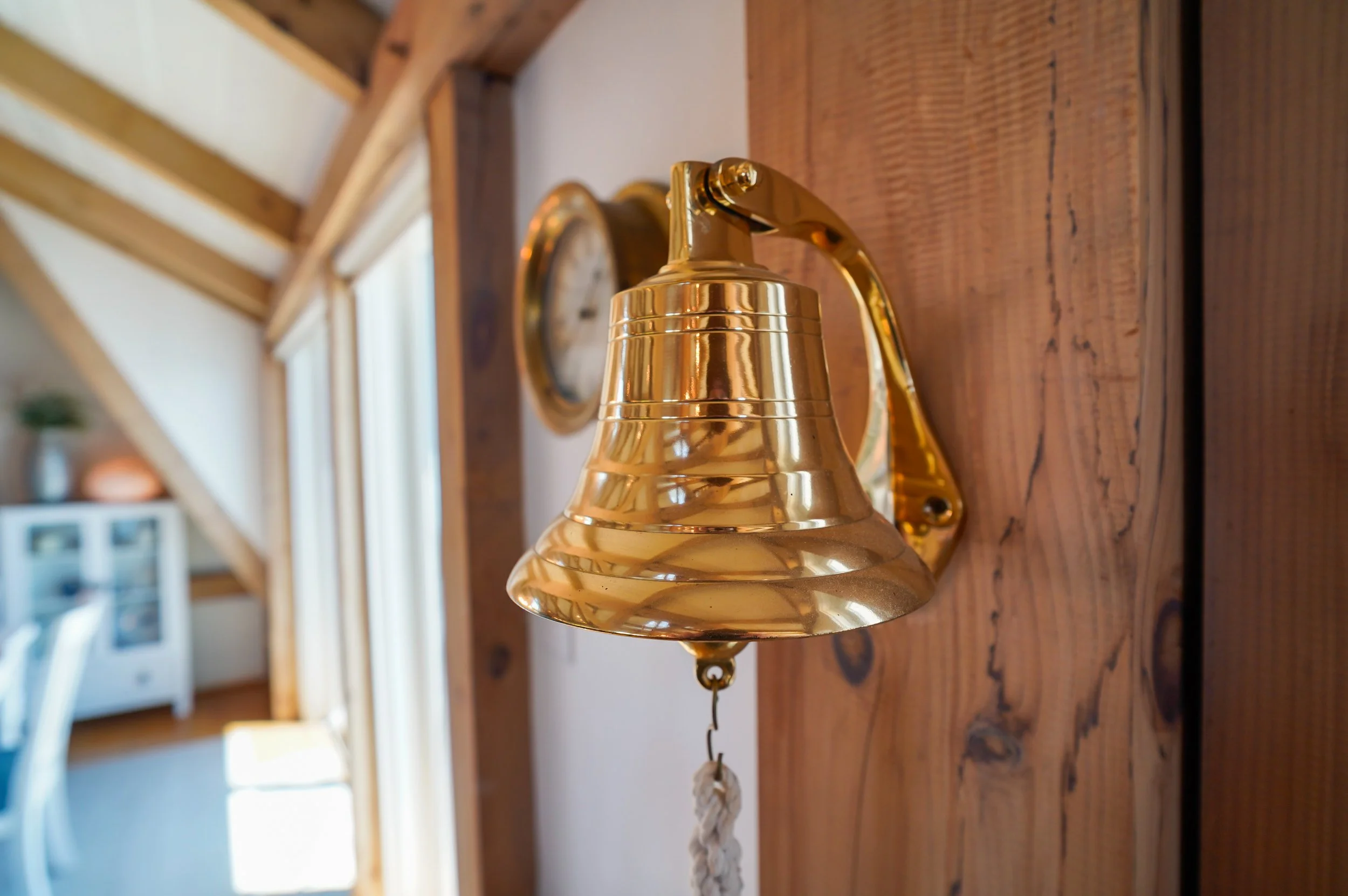 Gold-colored wall-mounted bell on a wooden wall in a cozy home interior.