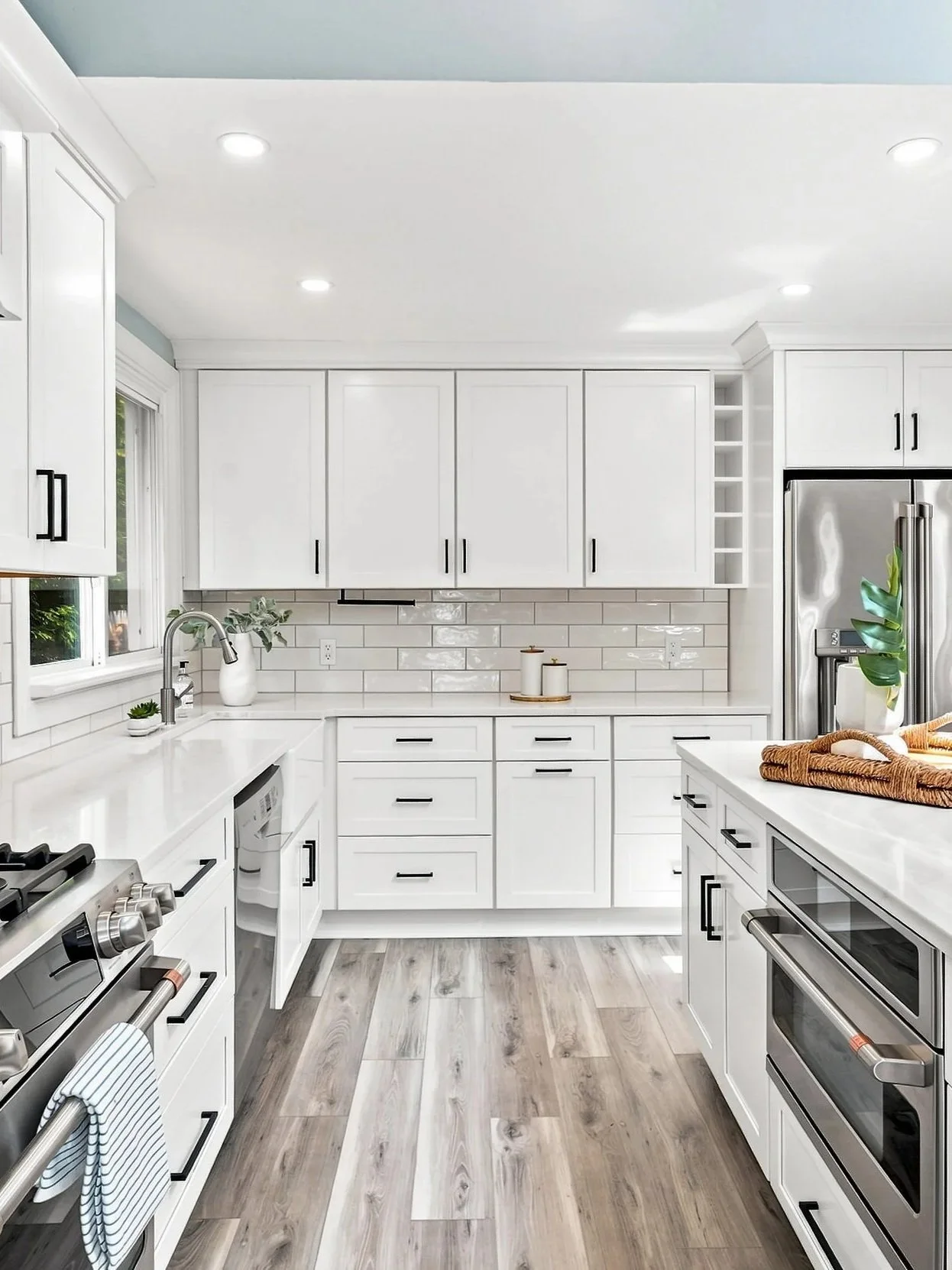 A modern kitchen with white cabinets, gray hardware, stainless steel appliances, a white subway tile backsplash, and wood-look flooring.