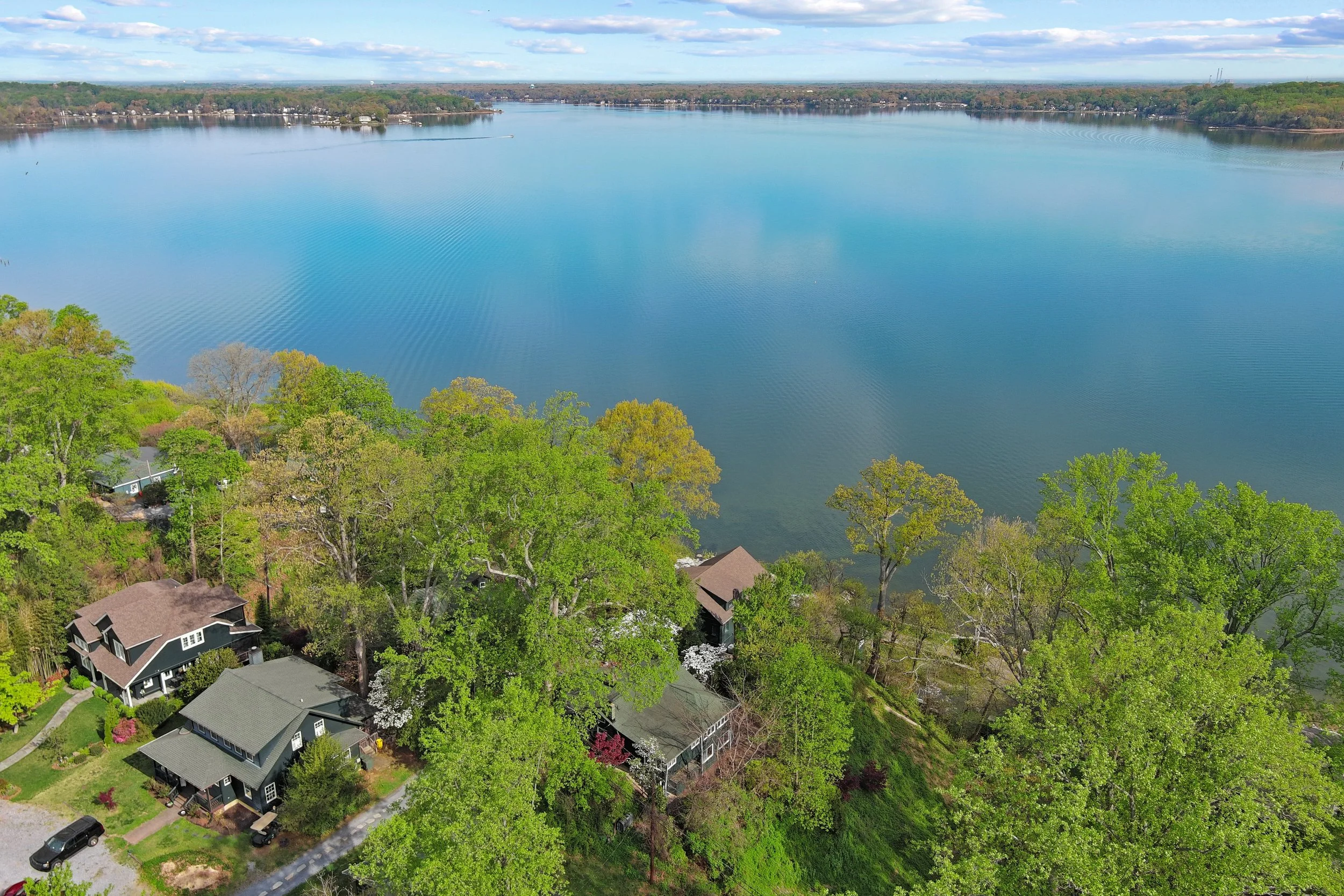 Aerial view of a large body of water, possibly a lake, with houses and trees along the shoreline and a partly cloudy sky overhead.