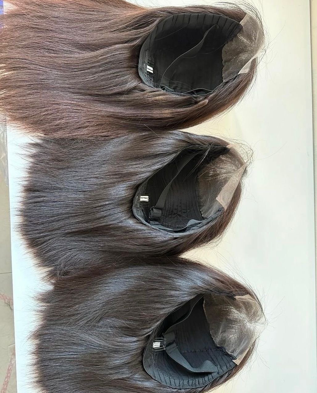 Three brown hairpieces with black hair net caps laid flat on a white surface.