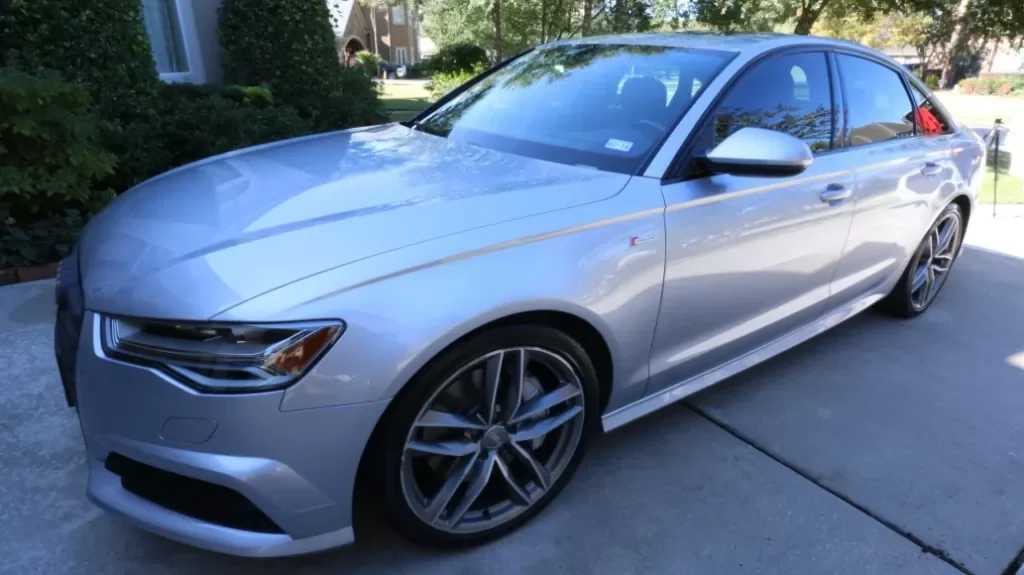 A silver sedan parked on a driveway with green bushes and trees in the background.