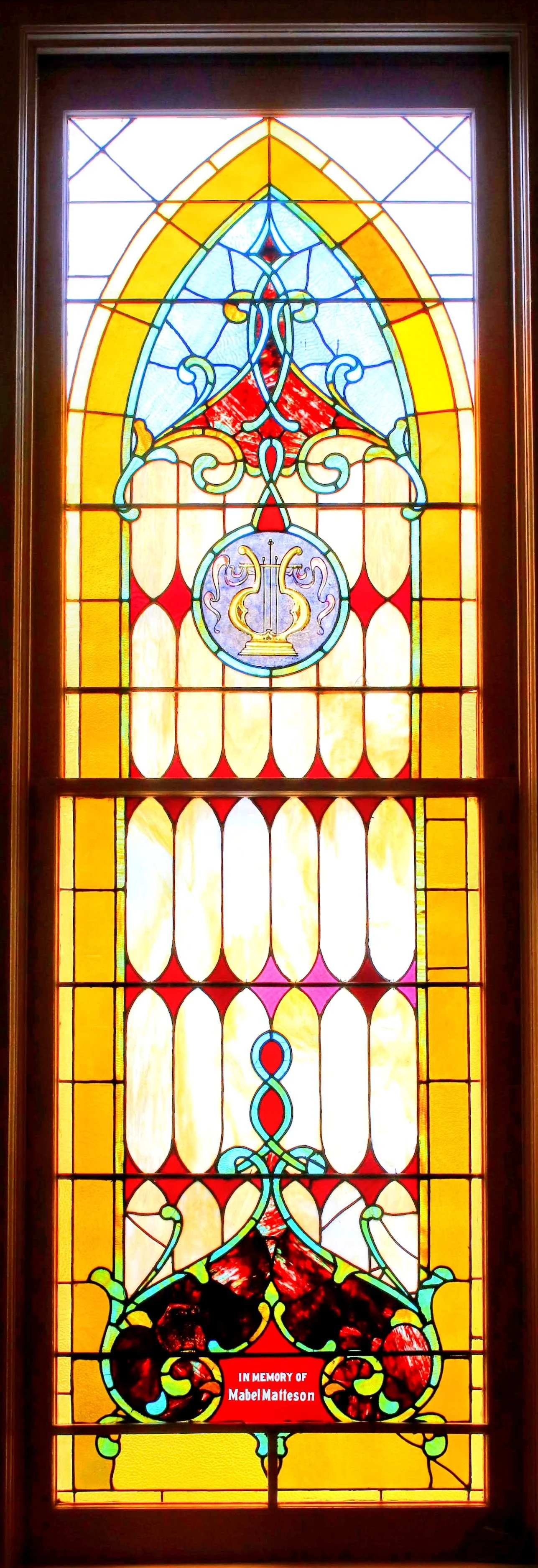 Colorful stained glass window with decorative patterns and memorial plaque for Mabel Matteson.