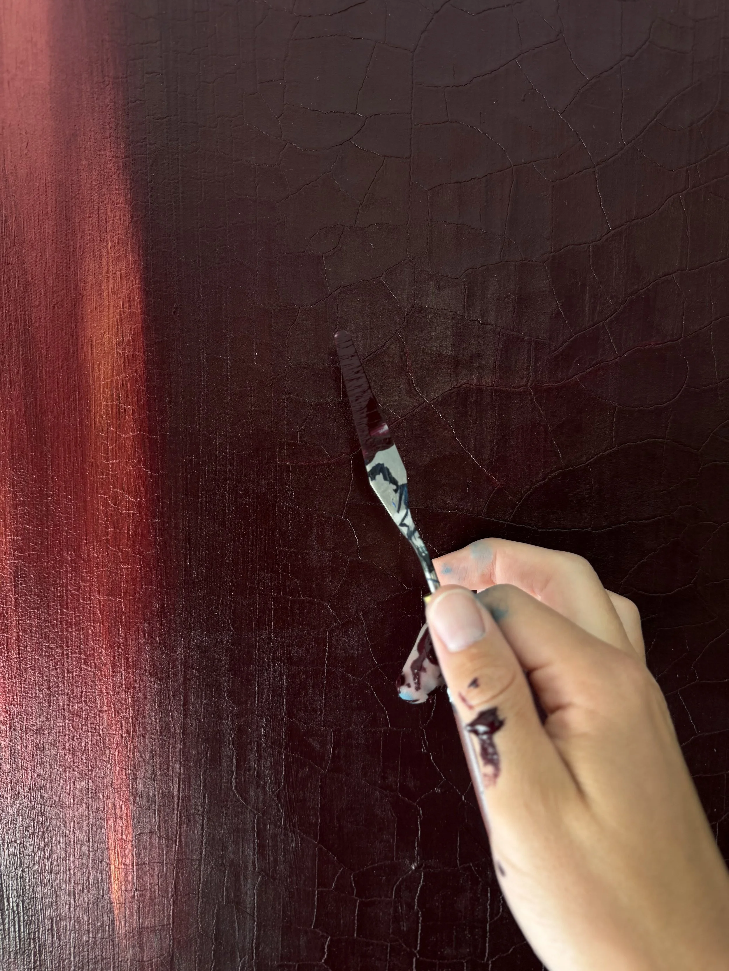 Person holding a paintbrush with a dark red and black textured surface in the background.