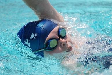 Young swimmer wearing a blue swim cap and goggles, swimming in a pool.