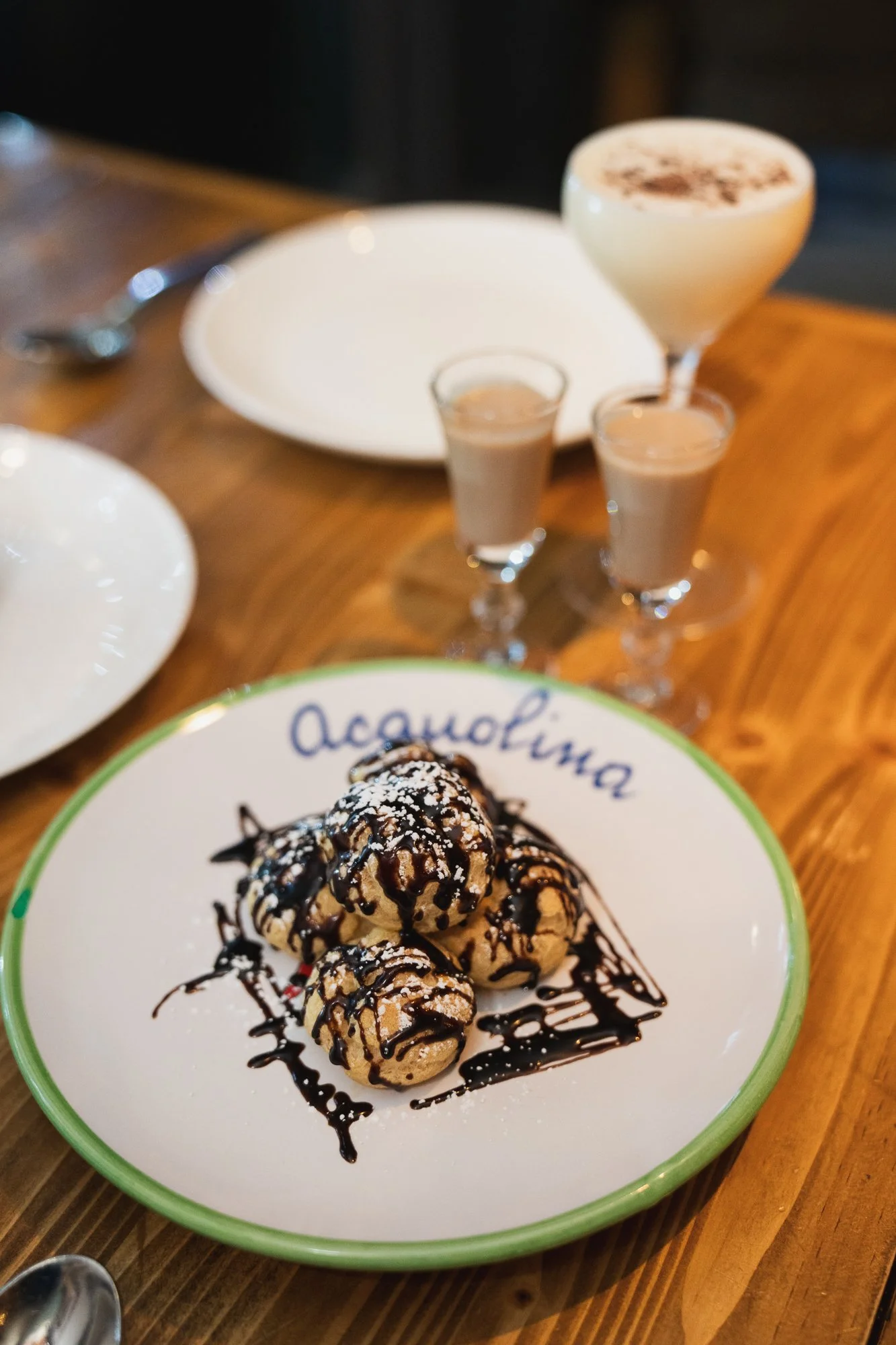 A dessert dish featuring scoops of ice cream drizzled with chocolate sauce on a white plate with a green rim, with the word 'Oceania' visible, on a wooden table.