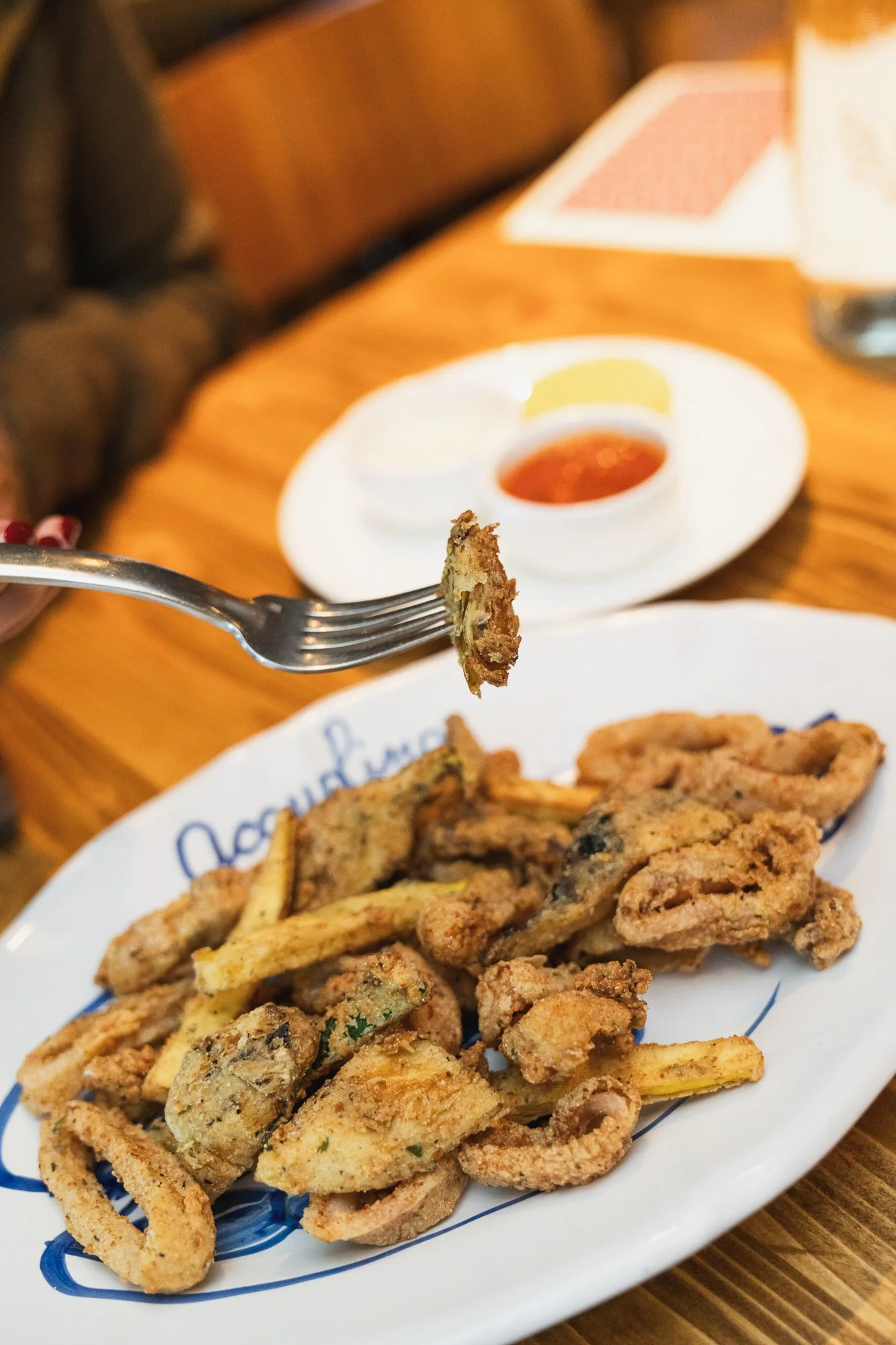 Fried calamari rings on a white oval plate with a side of lemon wedge and dipping sauce, placed on a wooden table.