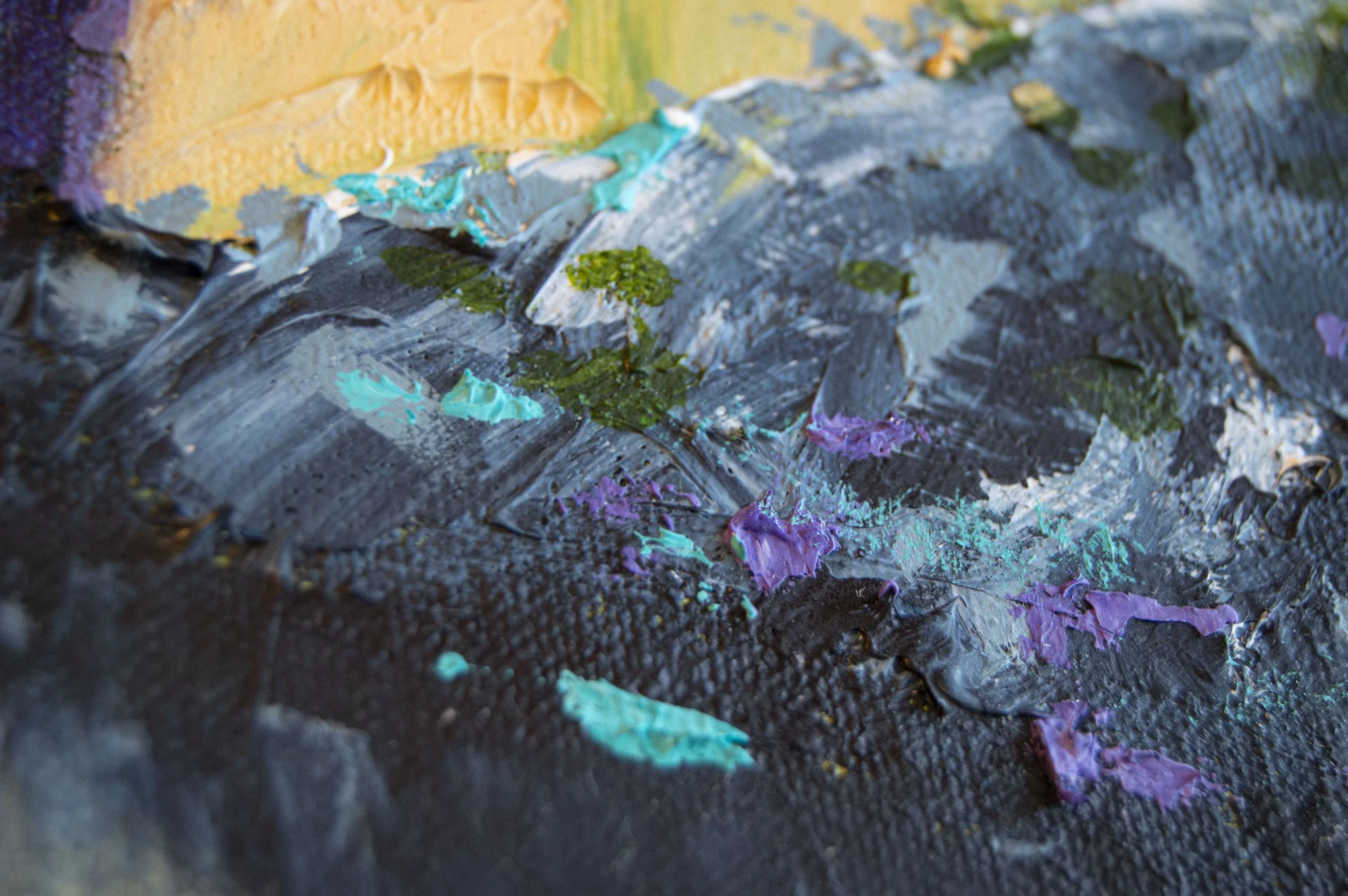 Close-up of an abstract painting with thick, textured strokes of dark gray and black, accented with vibrant splashes of purple, blue, green, and yellow paint.
