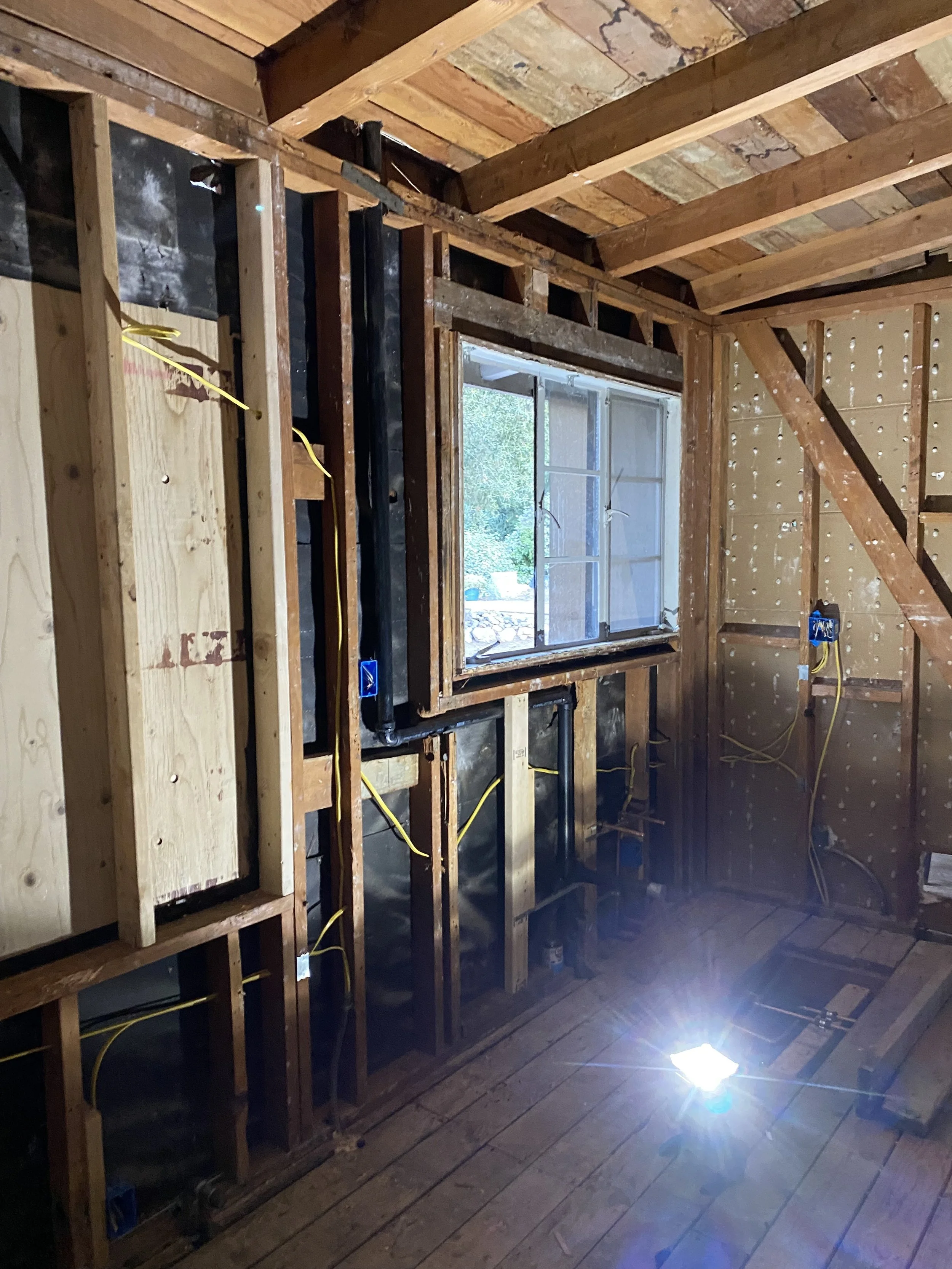 Unfinished interior wall with exposed wooden studs, electrical wiring, and a window in a room undergoing renovation or construction.