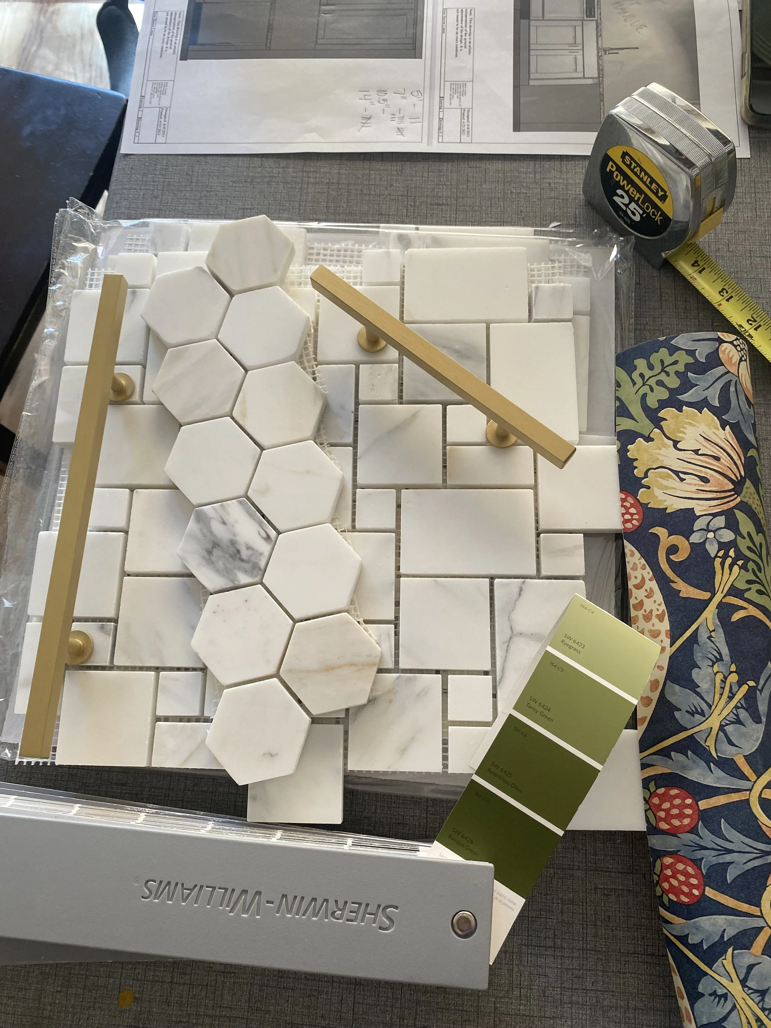 Samples of white marble tile and stone tile options displayed on a table at a store, with a yellow measuring tape and a color swatch card.