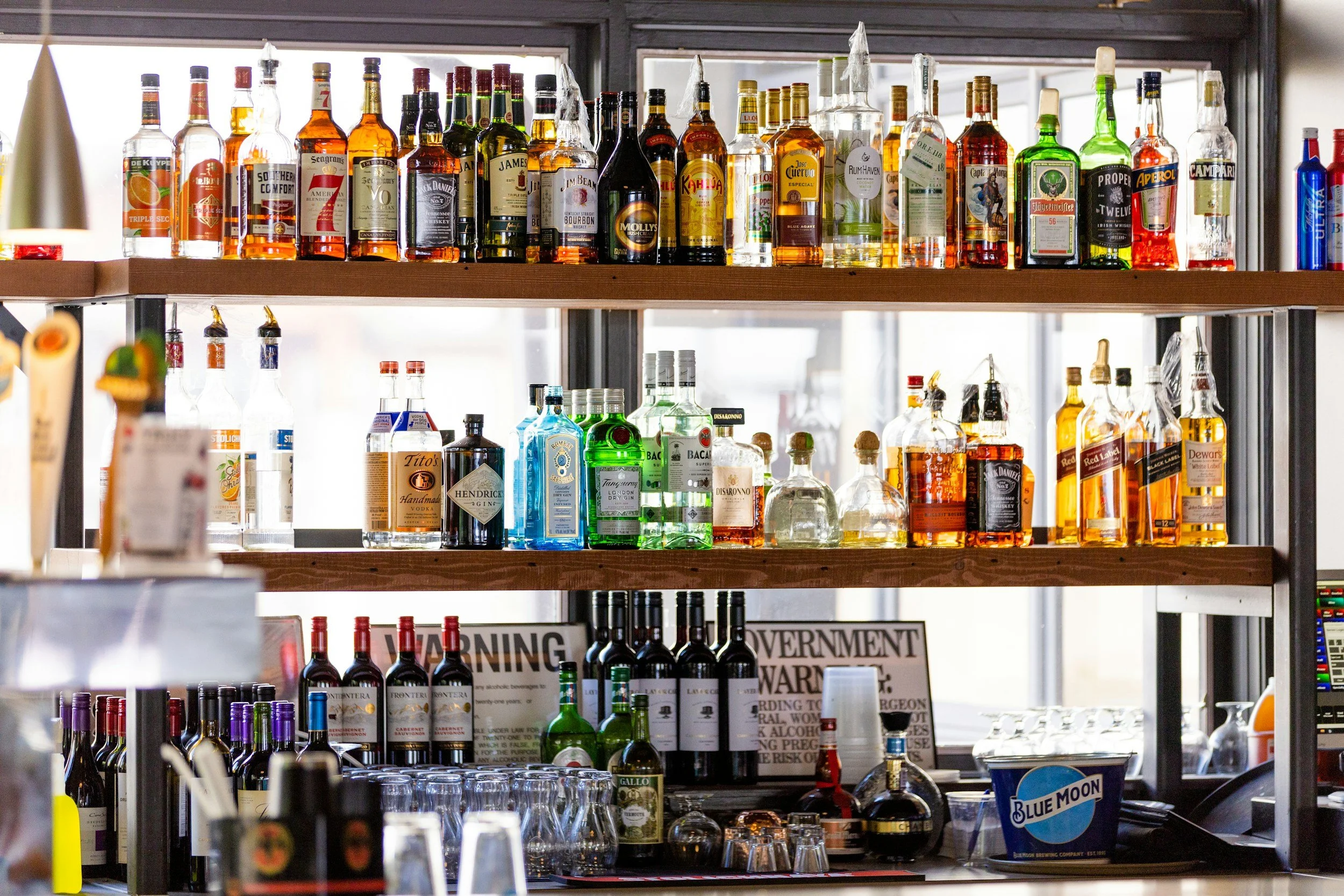 Shelves filled with various bottles of alcohol, including whiskey, vodka, gin, and rum, in a bar setting.