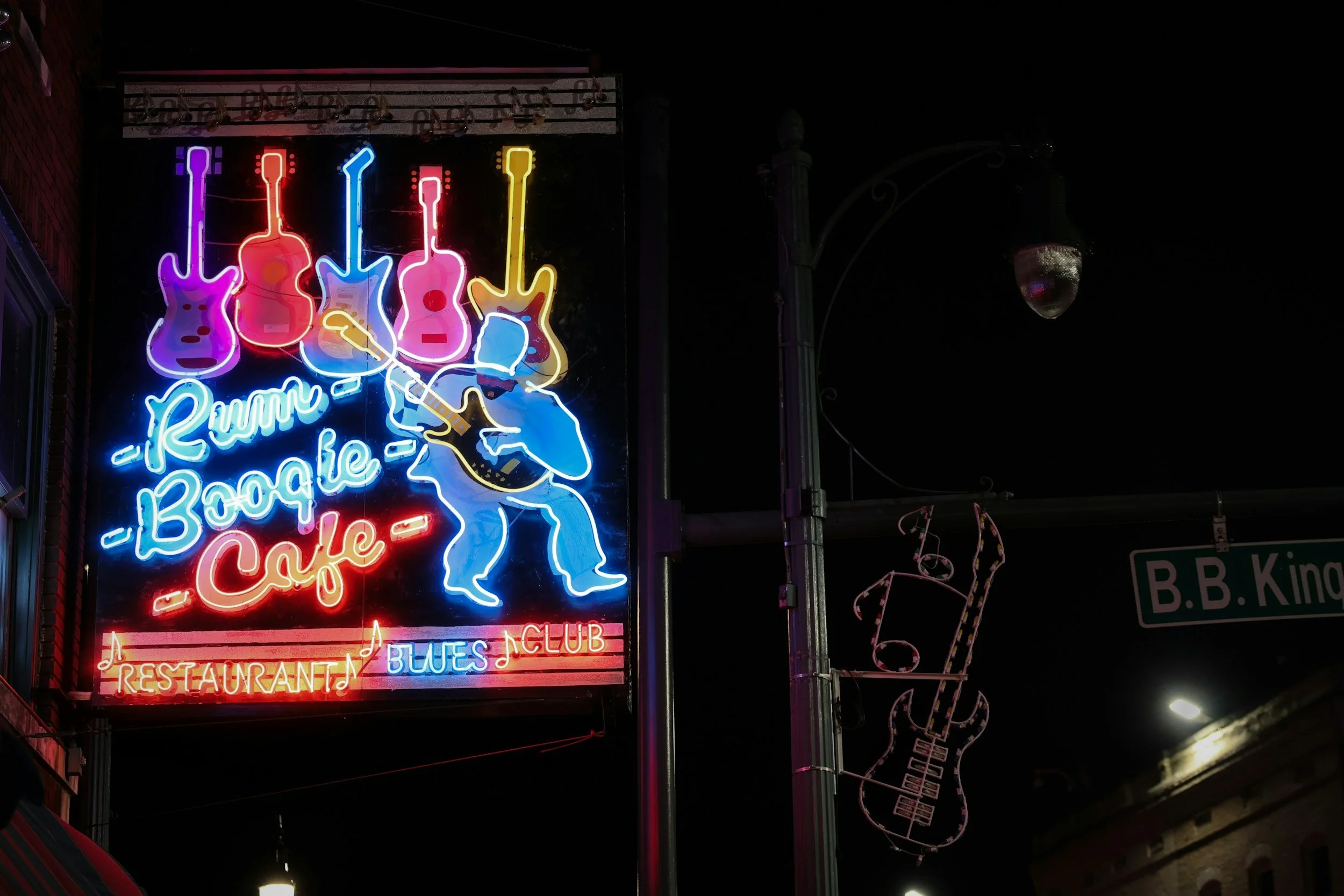 Neon sign advertising a blues club with guitars, a hand, and musical notes, indicating a restaurant and bar.
