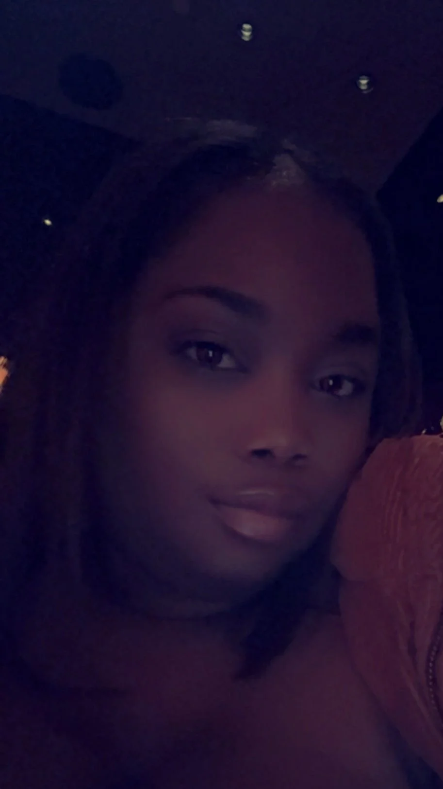 Close-up of a woman with dark hair and makeup, in a dimly lit setting.