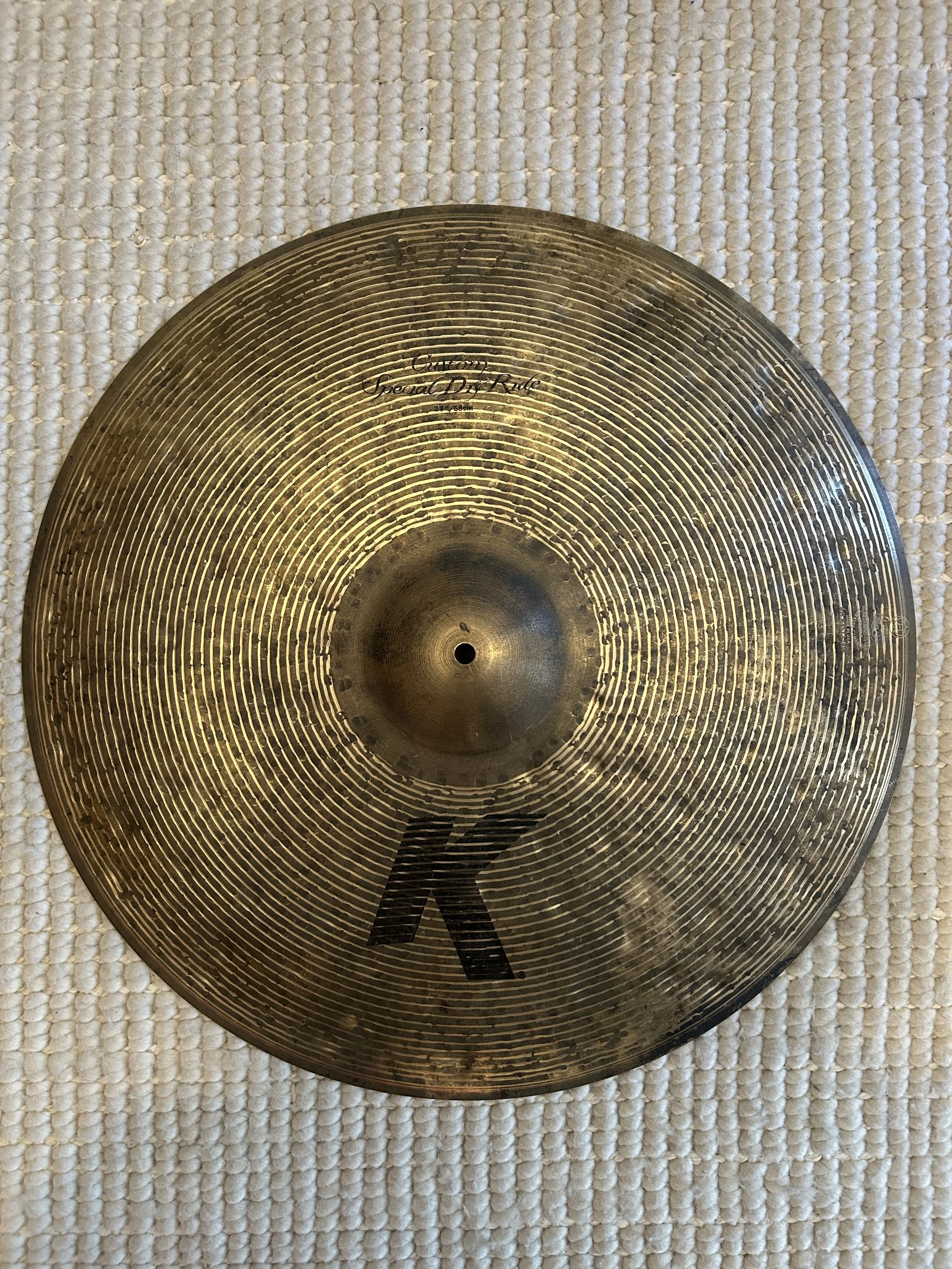A large metallic cymbal with black text and logo placed on a textured beige carpet.
