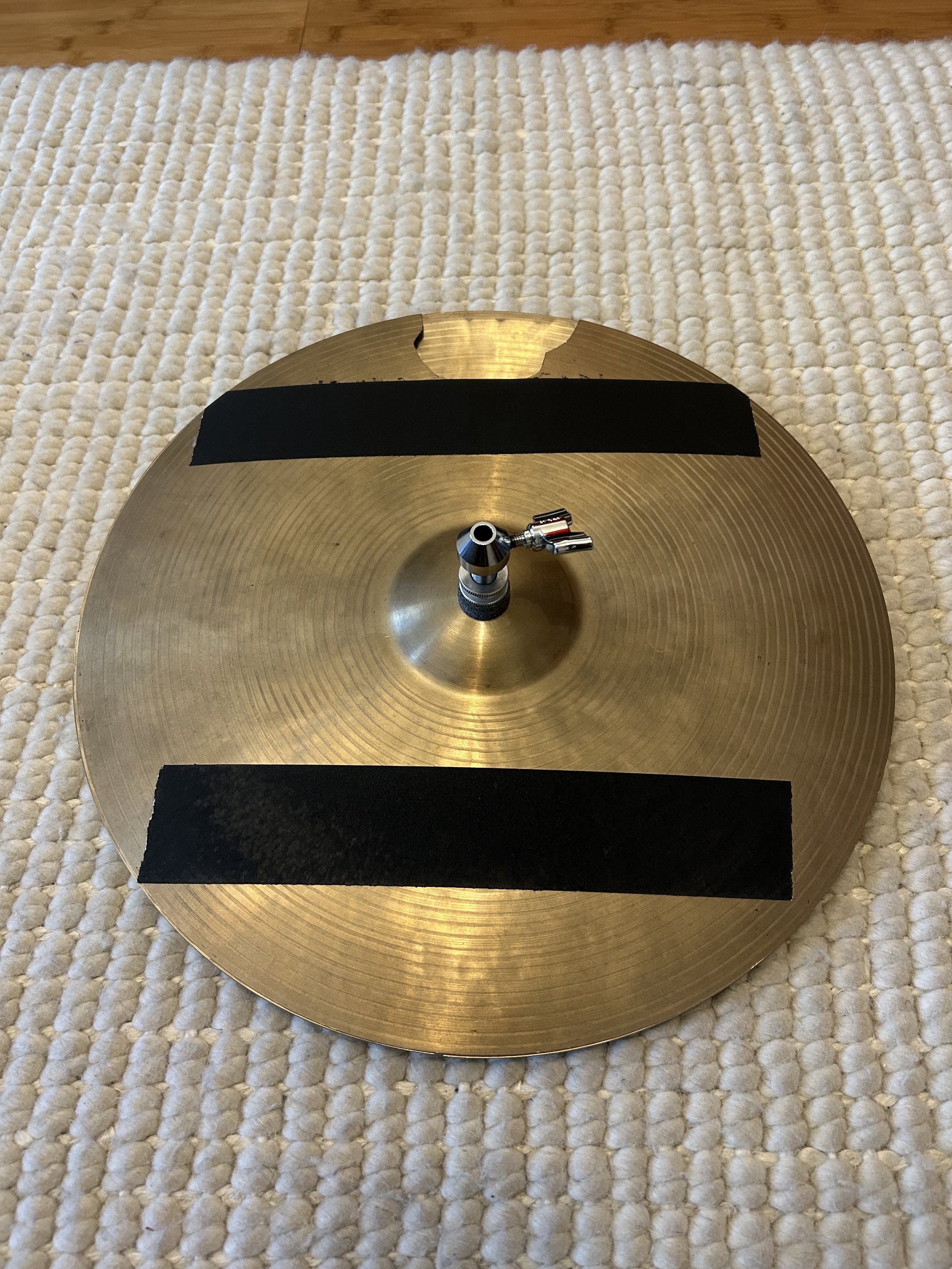 A cymbal with black tape covering most of the surface, placed on a textured white rug.