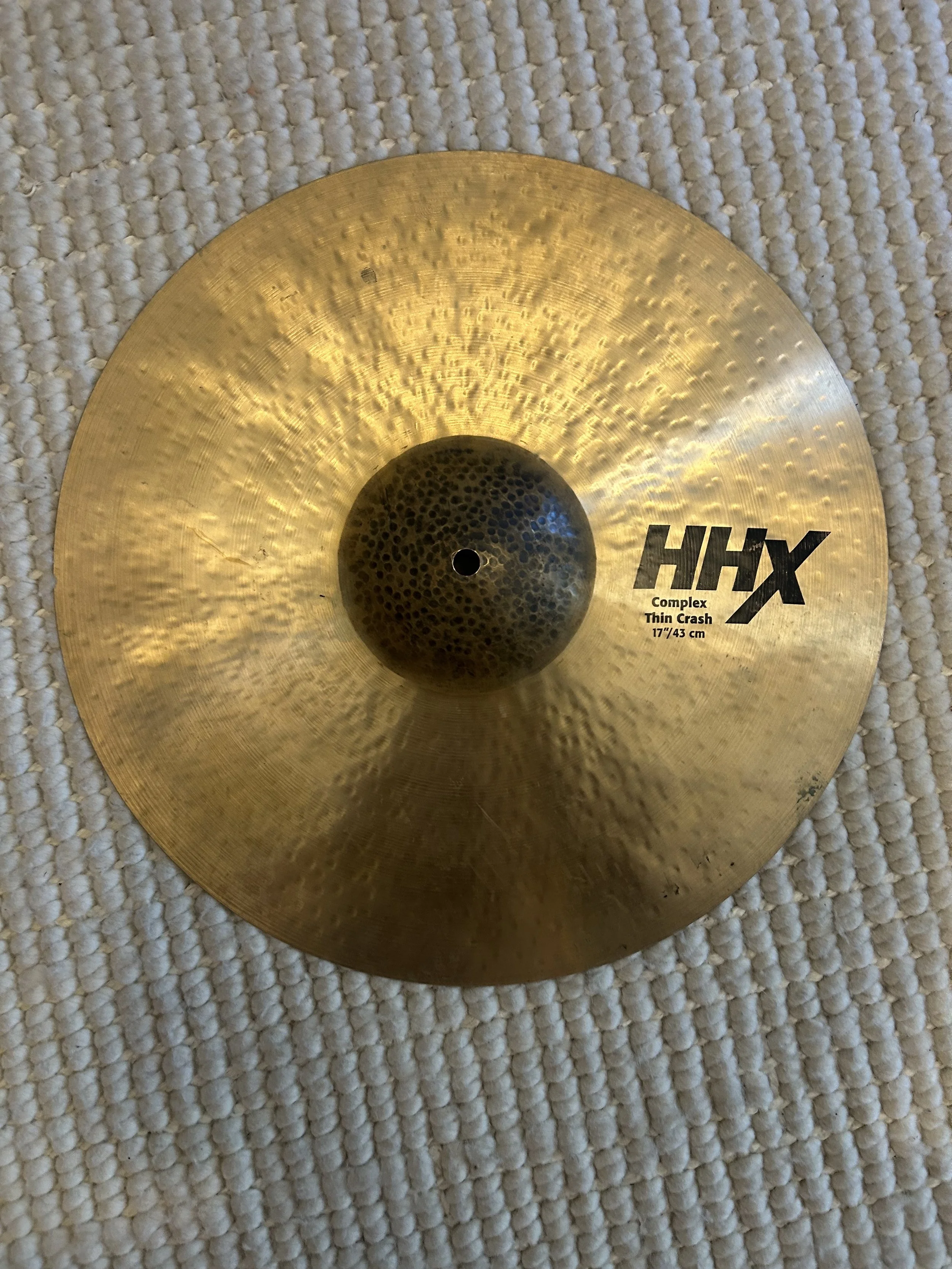A Zildjian cymbal, 17 inches, gold-colored, with the brand name and specifications printed on it, resting on a textured white surface.