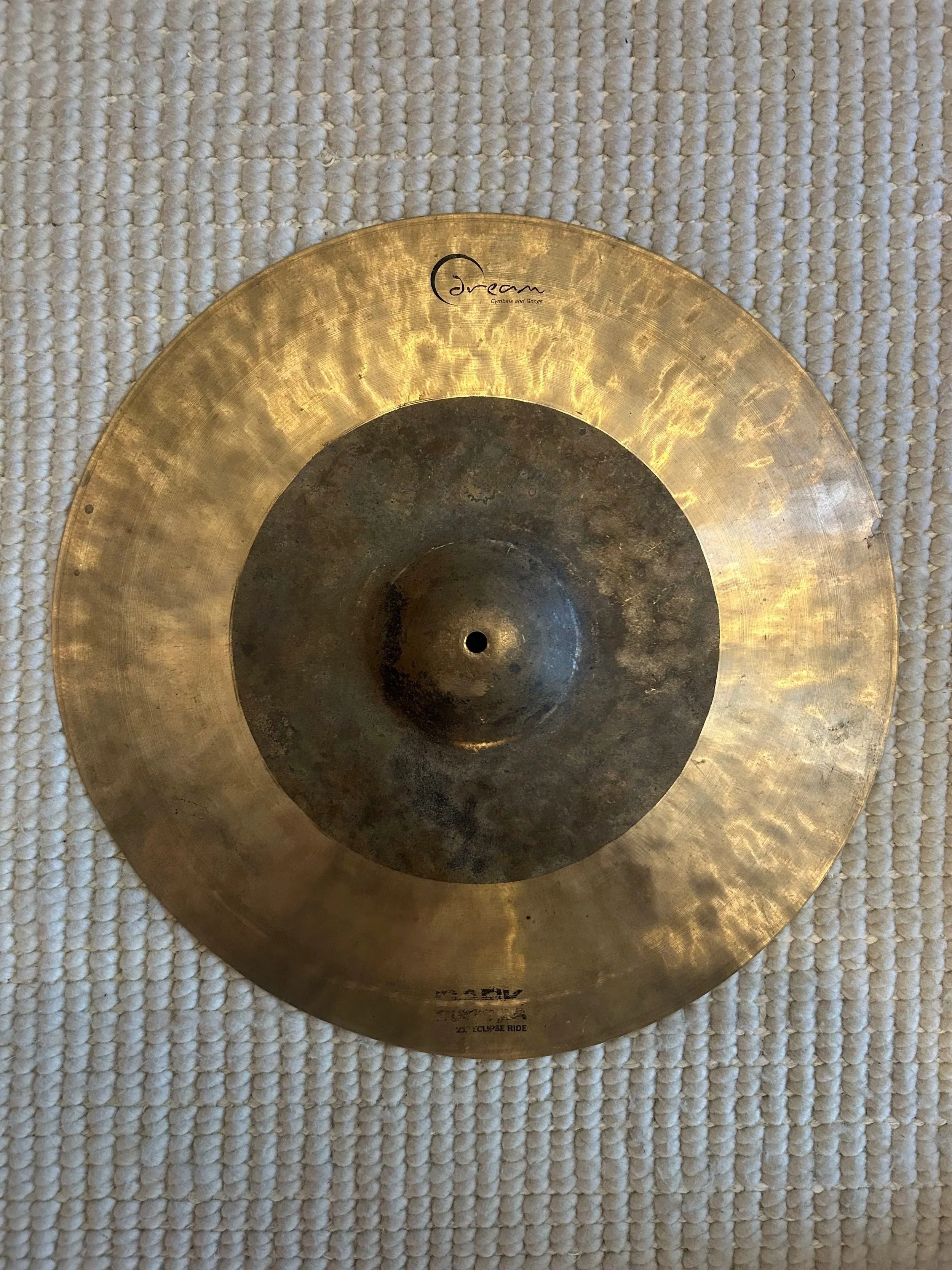 A golden cymbal with the words 'Dream Cymbals and Gongs' printed on it, resting on a textured white surface.